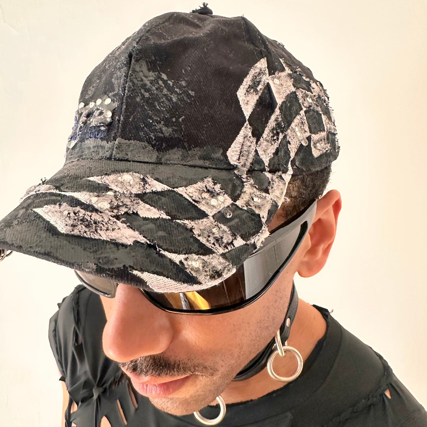 Checkerboard detail ofnASTROBOI* Speed Racing black and white checkered utility hat with resin-set rhinestones, stainless steel piercings, and hand-painted detailing