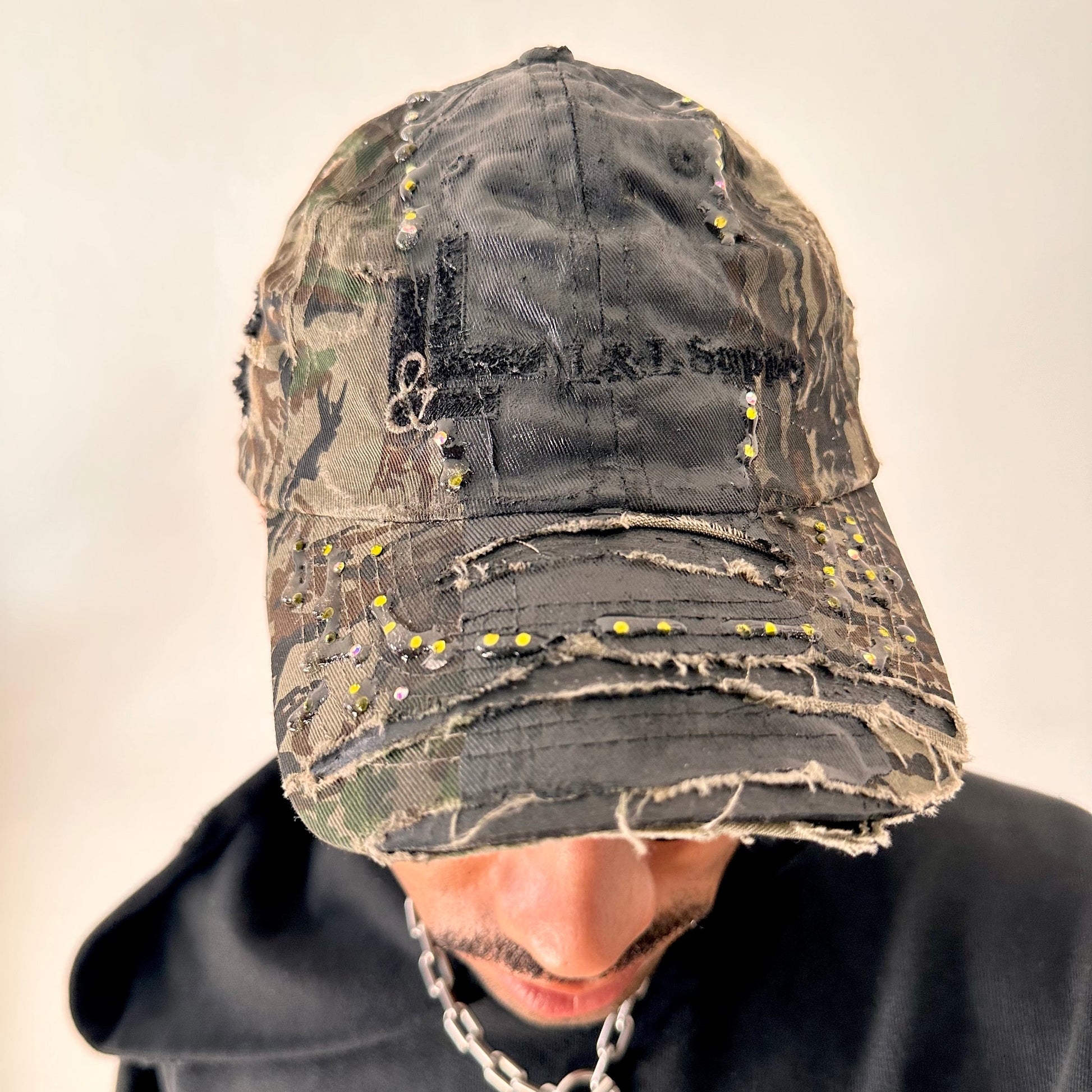 Front angled shot of ASTROBOI* L&L Supply green RealTree camo utility hat with purple and green rhinestones sealed in resin and black tattoo print detailing