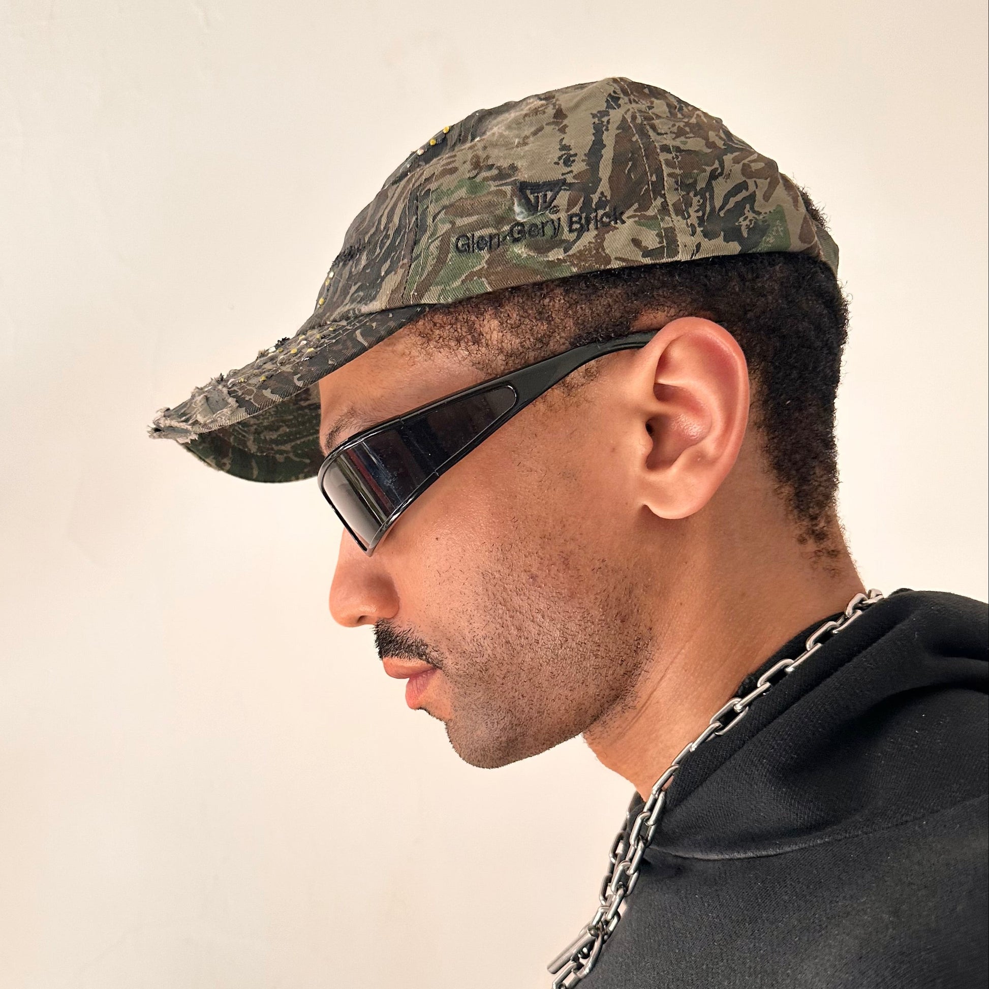 Left side of ASTROBOI* L&L Supply green RealTree camo utility hat with purple and green rhinestones sealed in resin and black tattoo print detailing