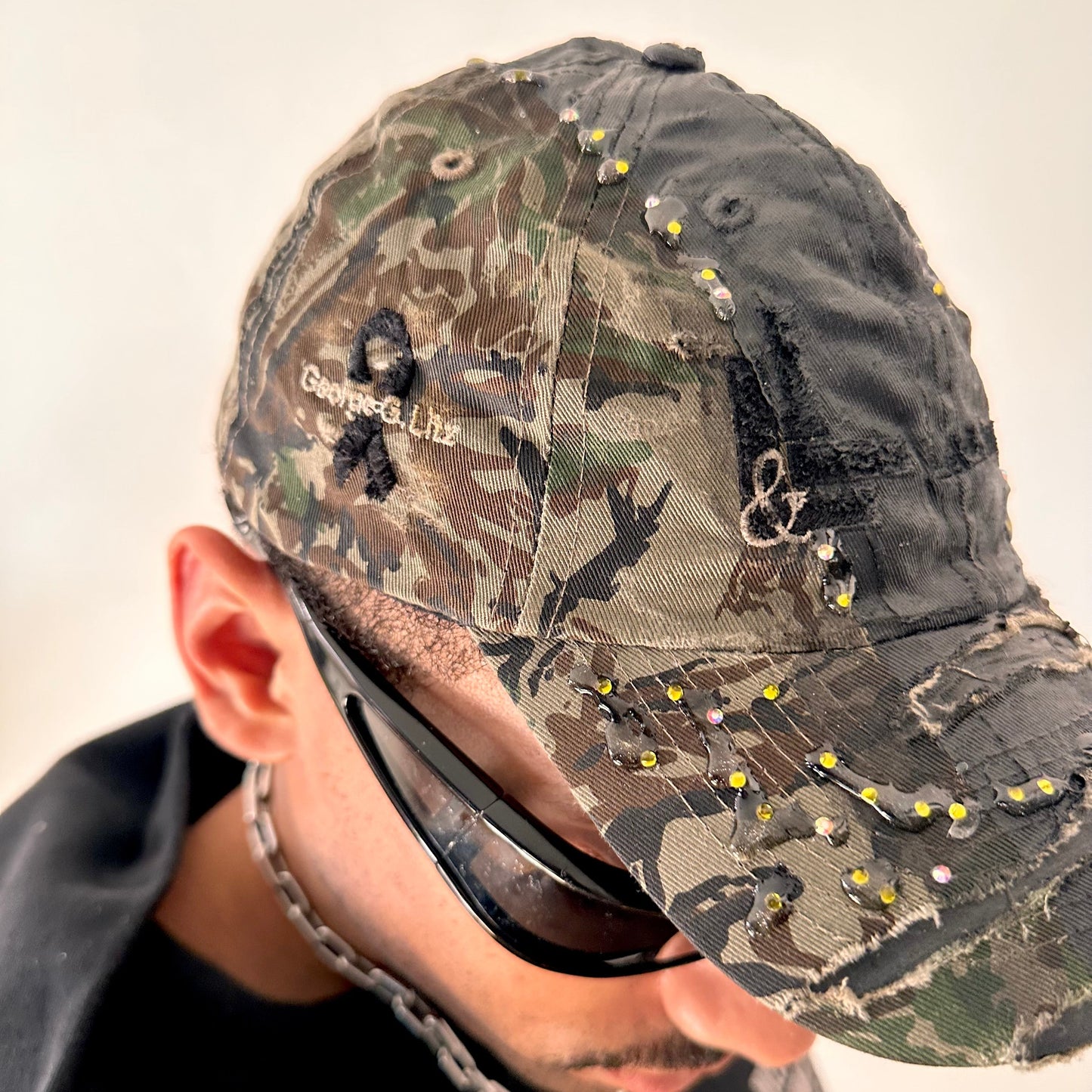 Front right detail on ASTROBOI* L&L Supply green RealTree camo utility hat with purple and green rhinestones sealed in resin and black tattoo print detailing