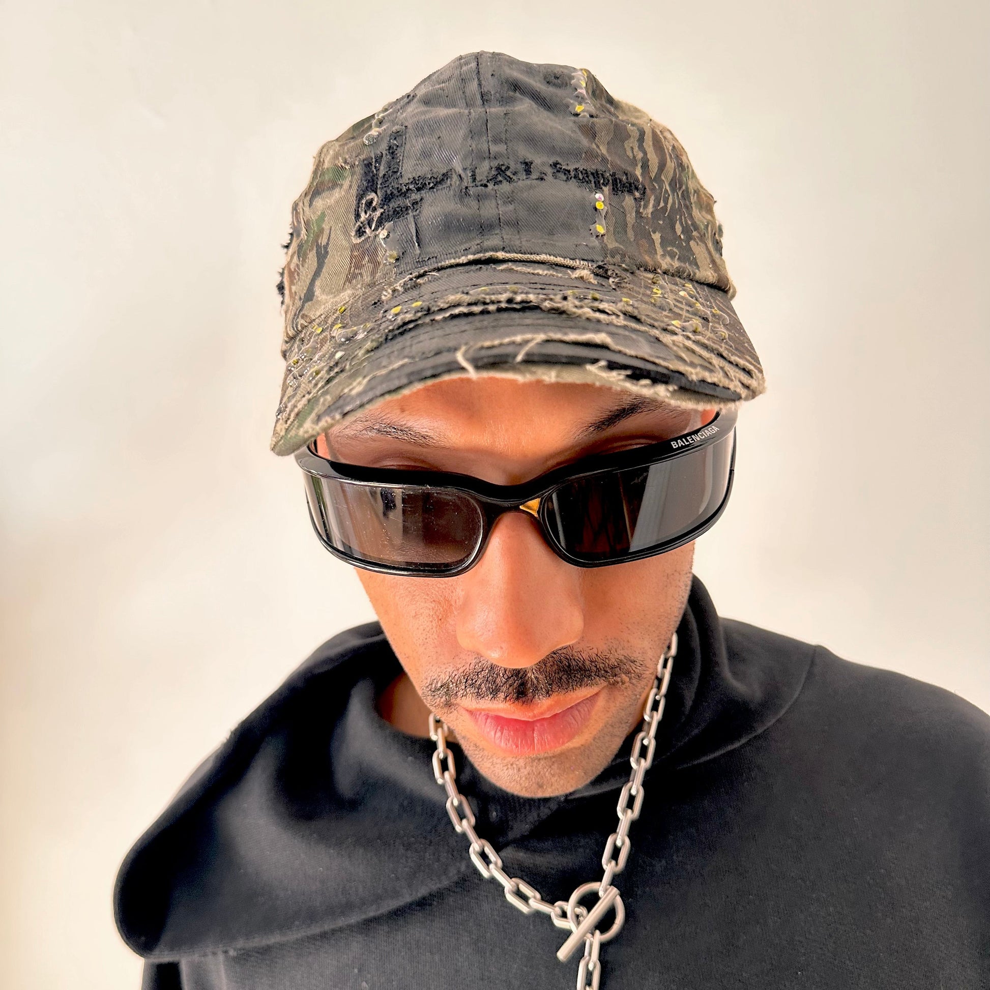 Overview of ASTROBOI* L&L Supply green RealTree camo utility hat with purple and green rhinestones sealed in resin and black tattoo print detailing