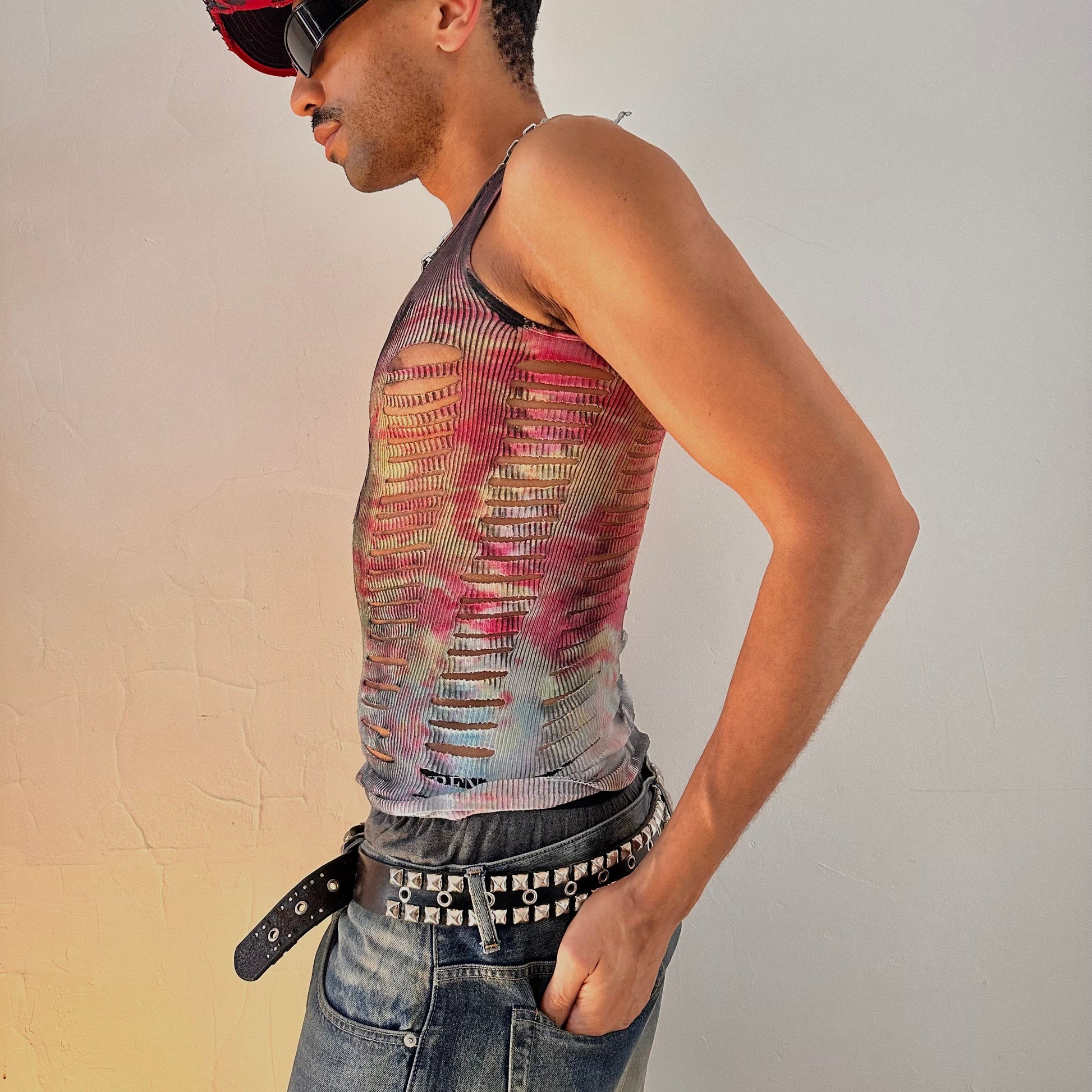 Person wearing a colorful distressed tank top and jeans with a plain background