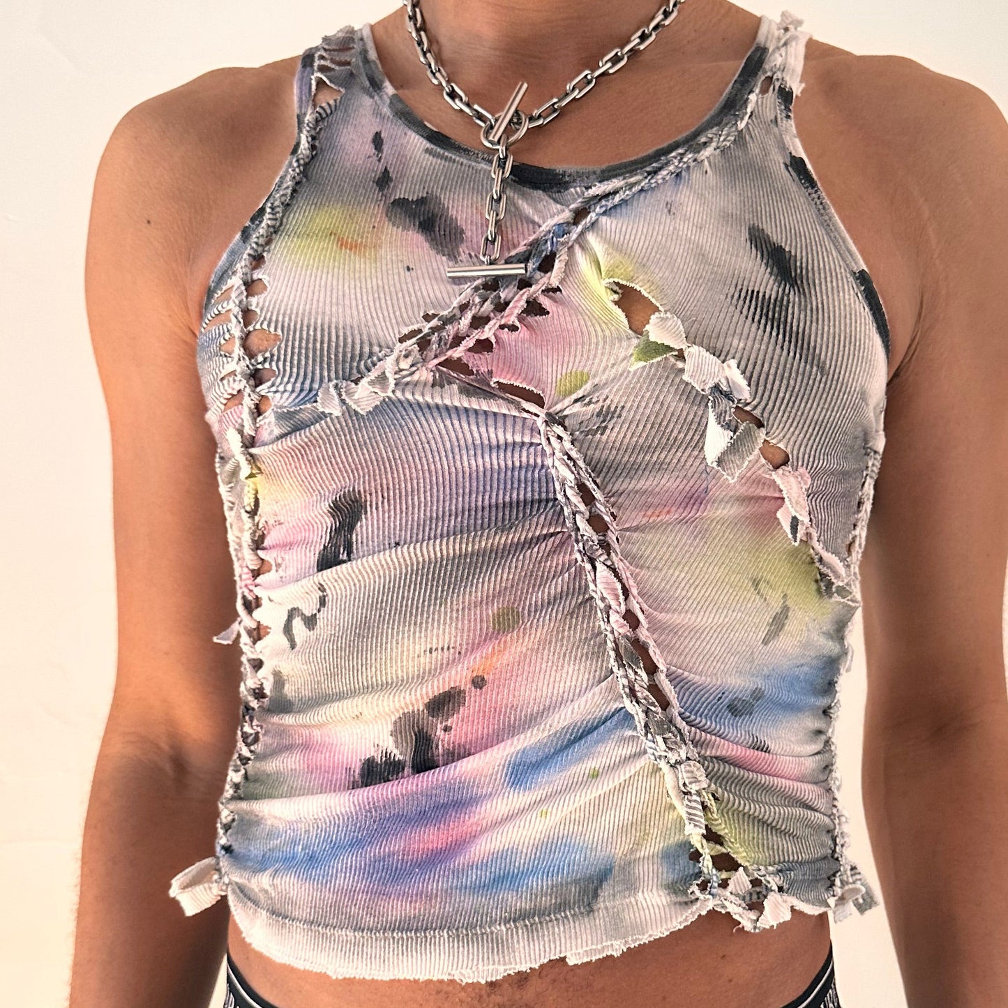 Close-up of ASTROBOI* x Calvin Klein 'Tri Color' showing hand-braided construction, slash detail, raw hem finish, and rainbow watercolor paint on white cotton.