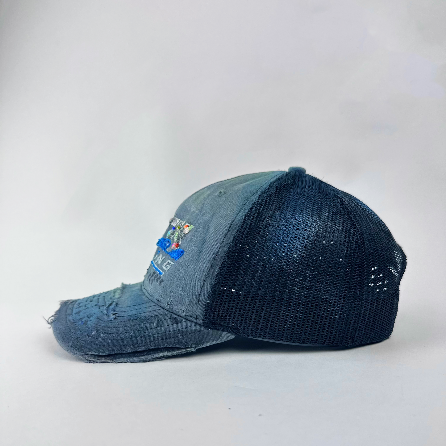 Left side detail of ASTROBOI* 'JFK Fishing' showing multicolor paint treatment and rhinestone embellishment detail on gray trucker cap.