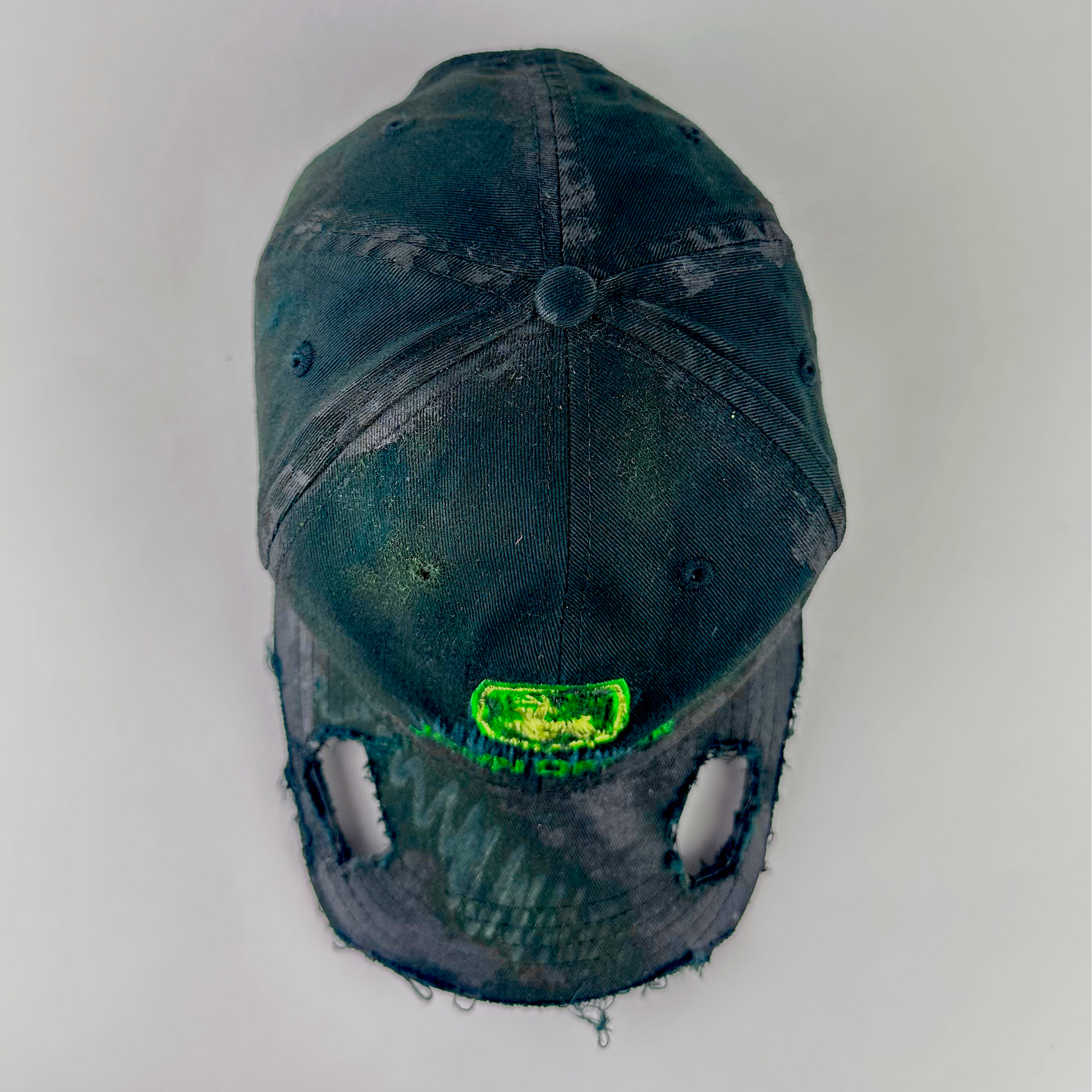 Top view of ASTROBOI* x John Deere 'Hyland' showing John Deere green and yellow logo patch and cut-out visor detail with custom paint treatment on black distressed fabric.