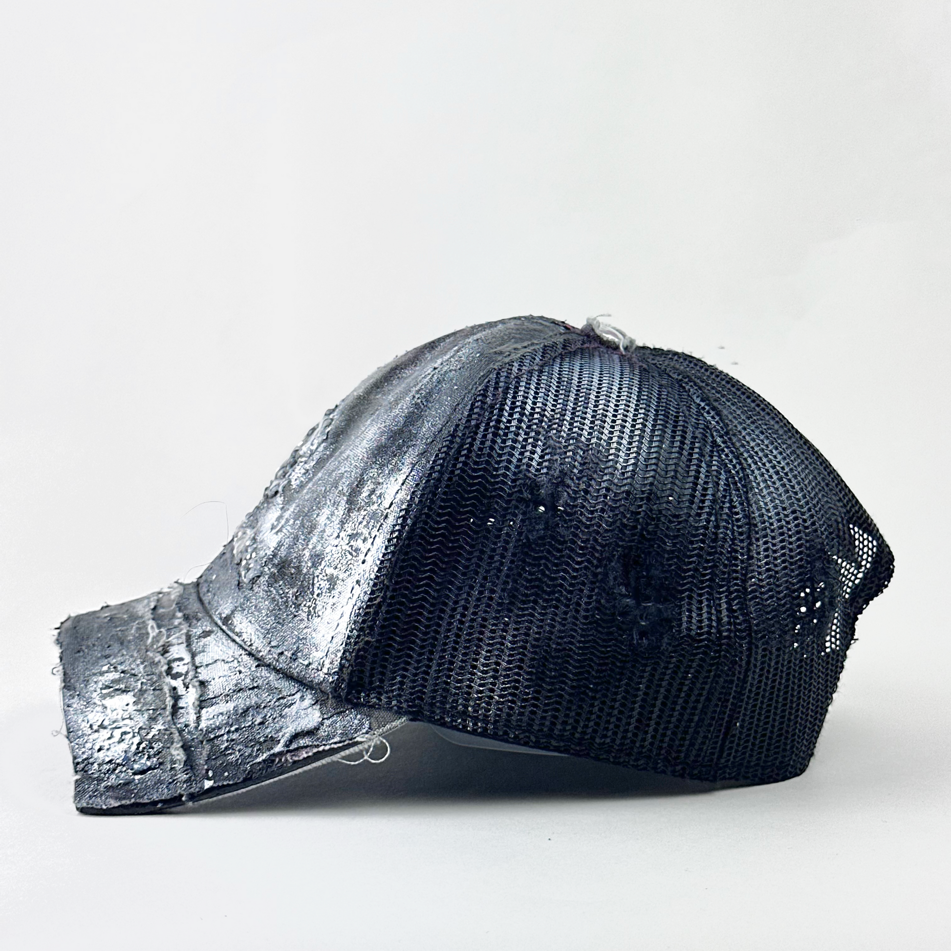 Left side detail of ASTROBOI* x John Deere 'Silver Surf' showing silver metallic treatment and deconstructed visor detail on gray digital camo trucker hat.