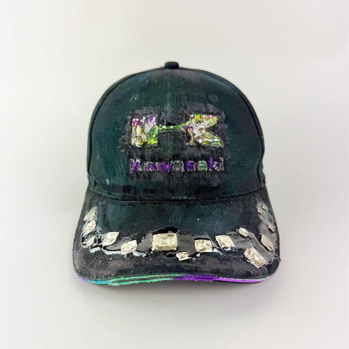 A distressed black baseball cap featuring a colorful, glittery Kawasaki logo and the word 'Kawasaki' in purple on the front, with rhinestone embellishments on the brim.