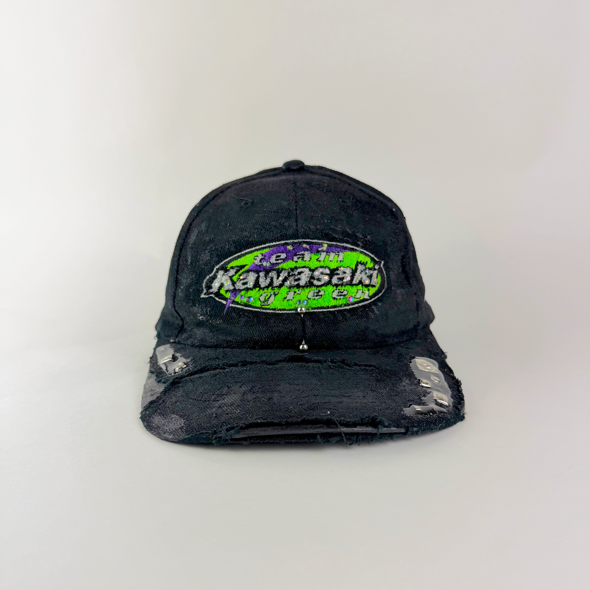 ASTROBOI* x Kawasaki 'Faust' black green and purple rhinestone studded cap with rhinestone-embellished Kawasaki logo, stainless steel piercing, and deconstructed visor, distanced shot front view.