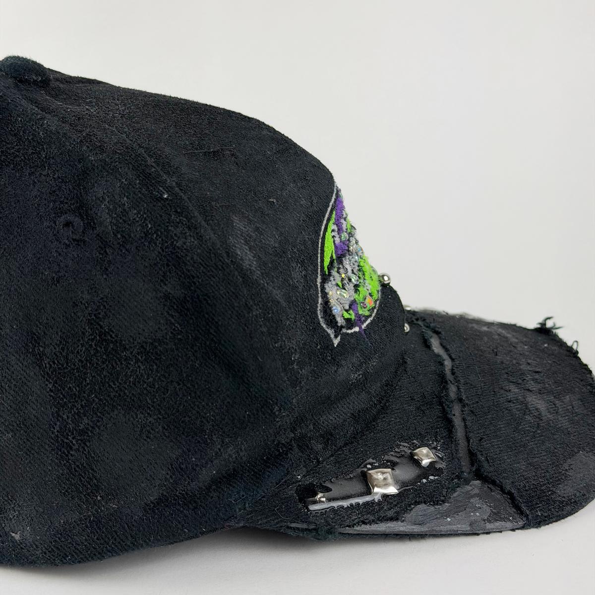 A black distressed baseball cap with a small embroidered patch on the side and a silver USB charging port attached to the brim, photographed on a light gray background.
