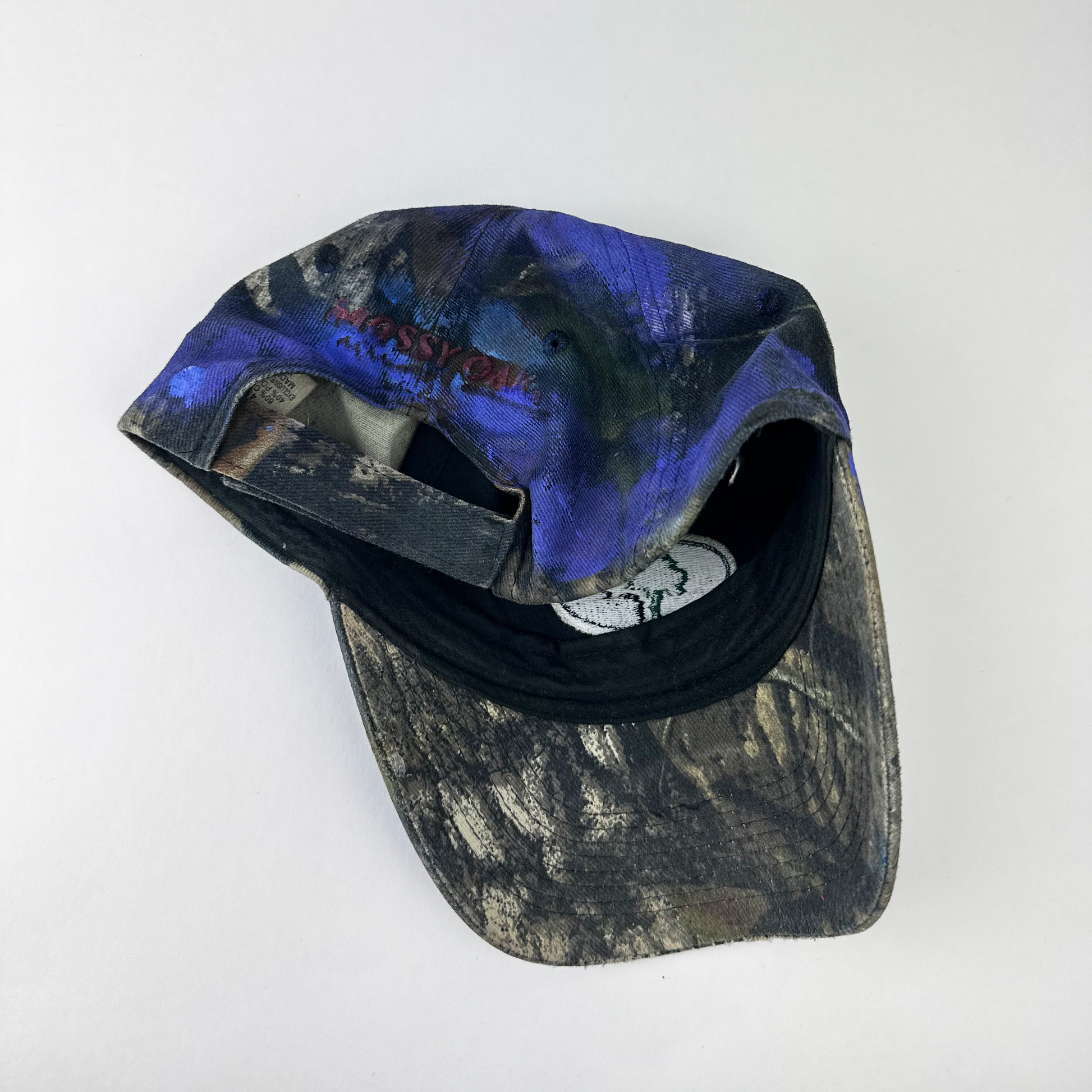 ASTROBOI* x Mossy Oak 'Ultraviolet' brown and purple camouflage hat, rear view showing embroidered Mossy Oak back logo and adjustable strap.
