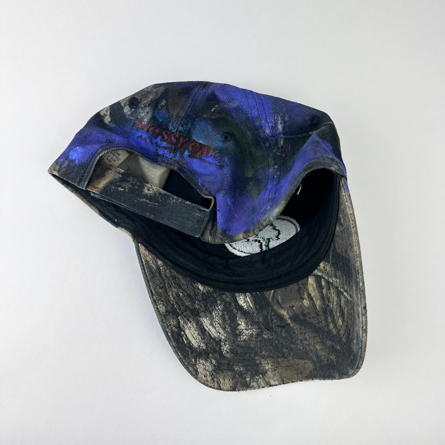 ASTROBOI* x Mossy Oak 'Ultraviolet' brown and purple camouflage hat, rear view showing embroidered Mossy Oak back logo and adjustable strap.