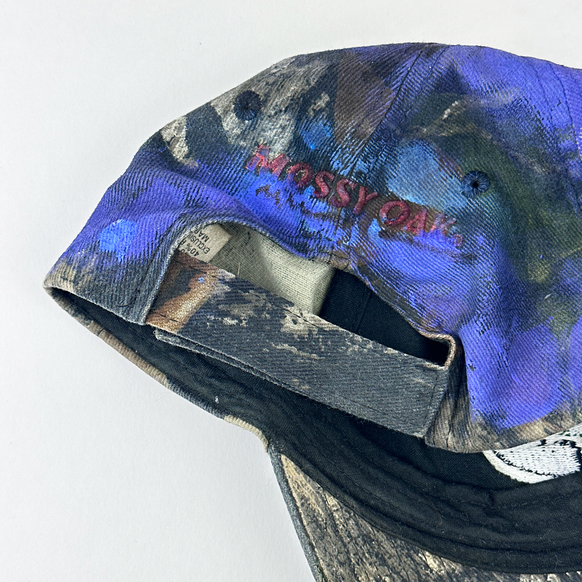 ASTROBOI* x Mossy Oak 'Ultraviolet' brown and purple camouflage hat, rear view showing embroidered Mossy Oak back logo and adjustable strap close up.