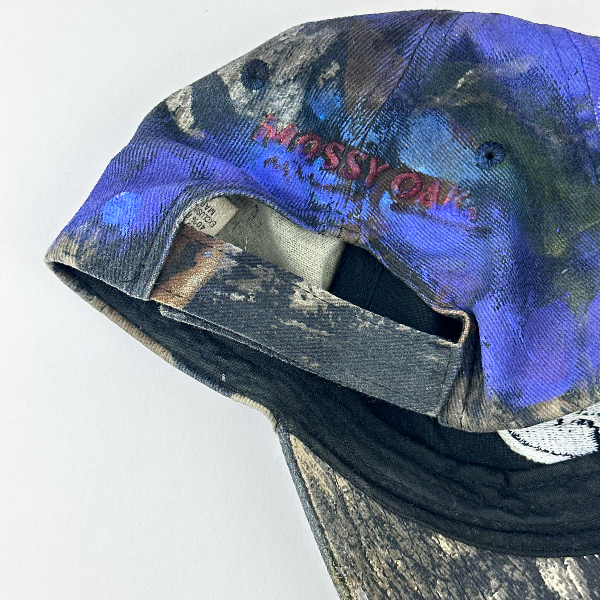 ASTROBOI* x Mossy Oak 'Ultraviolet' brown and purple camouflage hat, rear view showing embroidered Mossy Oak back logo and adjustable strap.