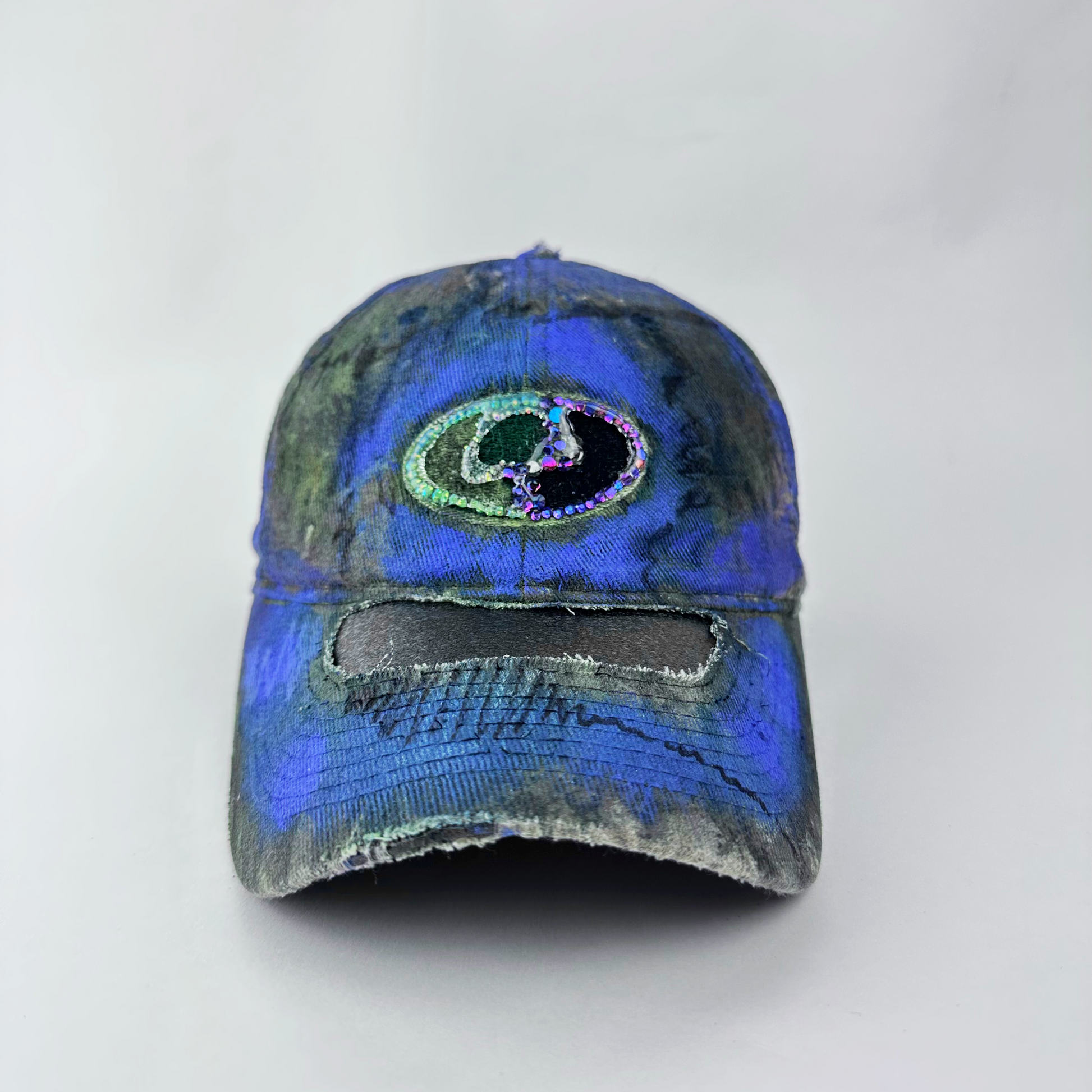 ASTROBOI* x Mossy Oak 'Ultraviolet' brown and purple Real Tree camouflage hat with rhinestone-embellished Mossy Oak logo at front, ultraviolet flowing paint treatment, and deconstructed visor, front view.
