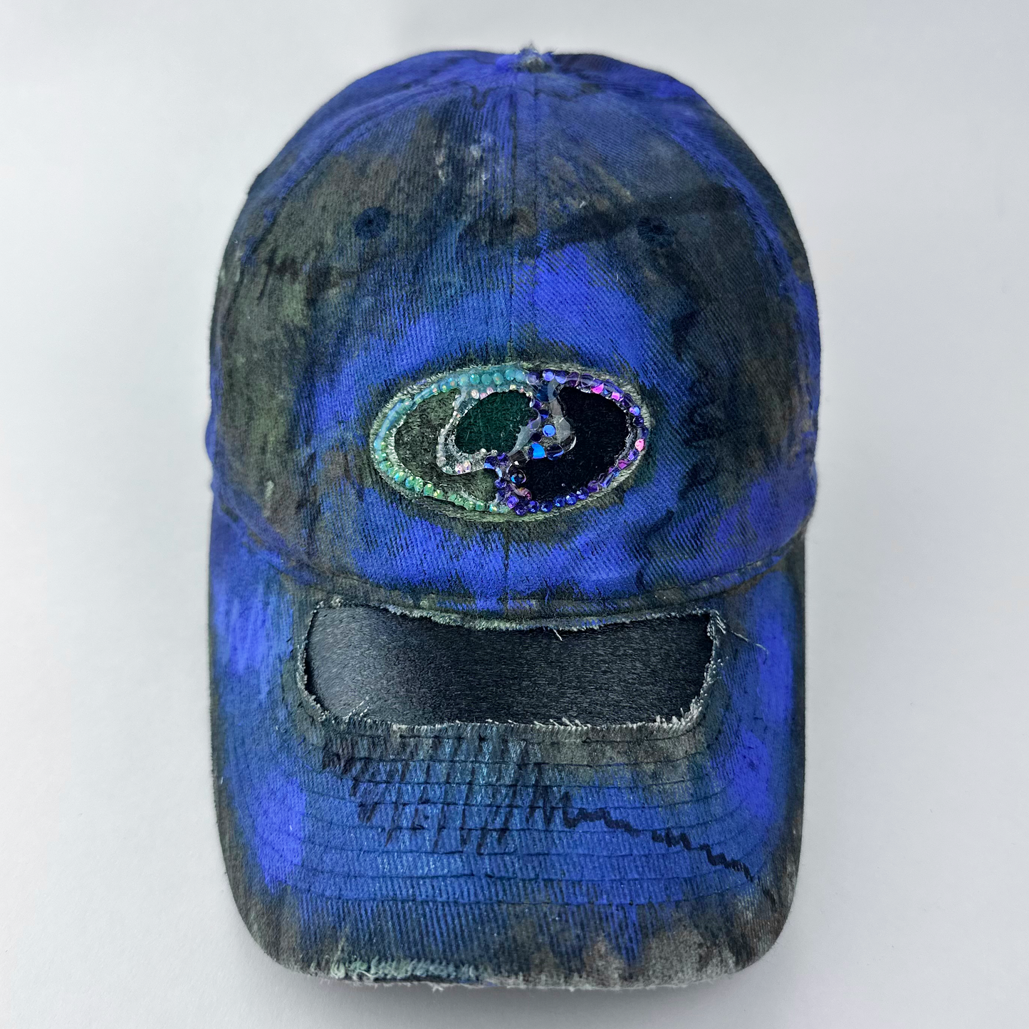 ASTROBOI* x Mossy Oak 'Ultraviolet' brown and purple Real Tree camouflage hat with rhinestone-embellished Mossy Oak logo at front, ultraviolet flowing paint treatment, and deconstructed visor, front view cover image.