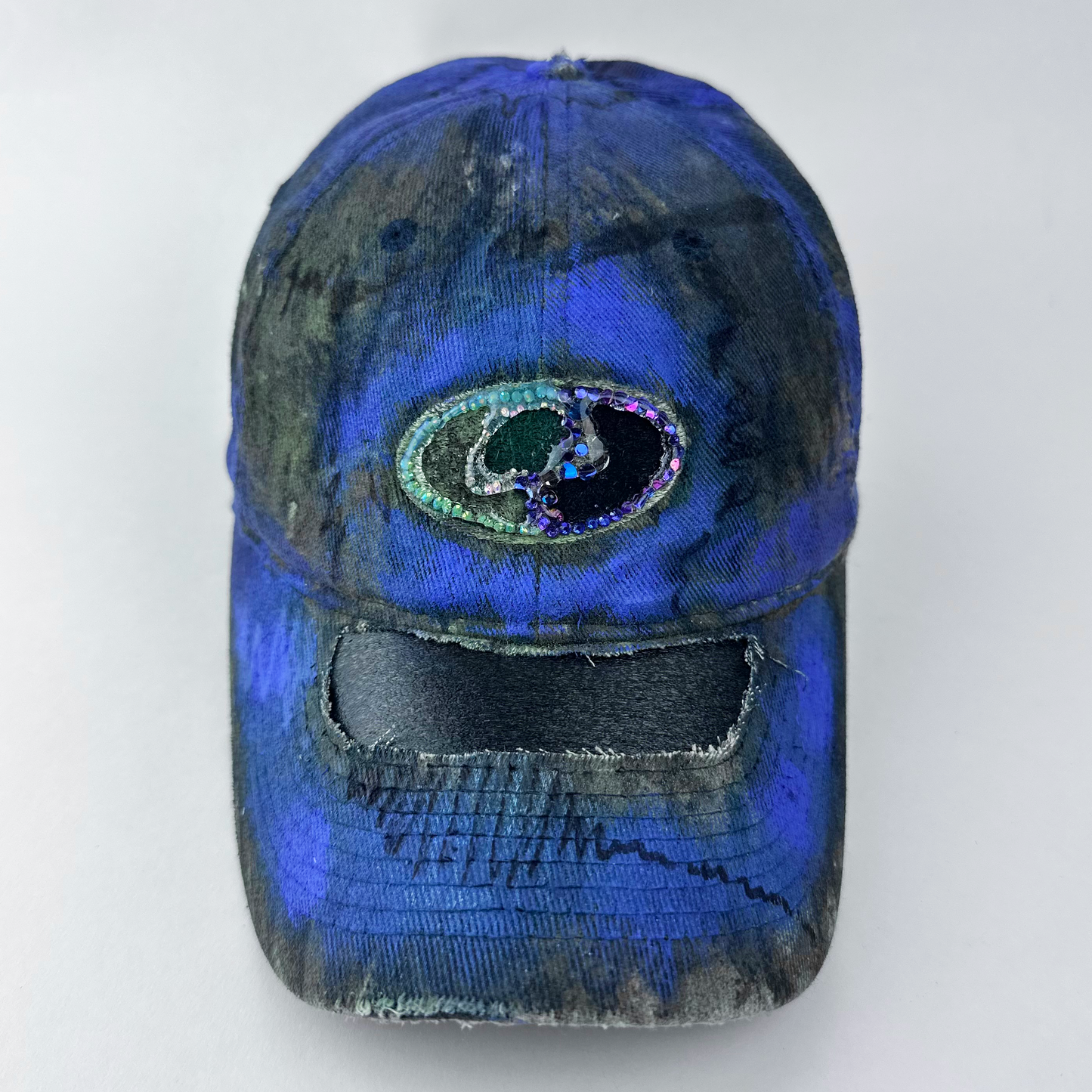 ASTROBOI* x Mossy Oak 'Ultraviolet' brown and purple Real Tree camouflage hat with rhinestone-embellished Mossy Oak logo at front, ultraviolet flowing paint treatment, and deconstructed visor, front view.