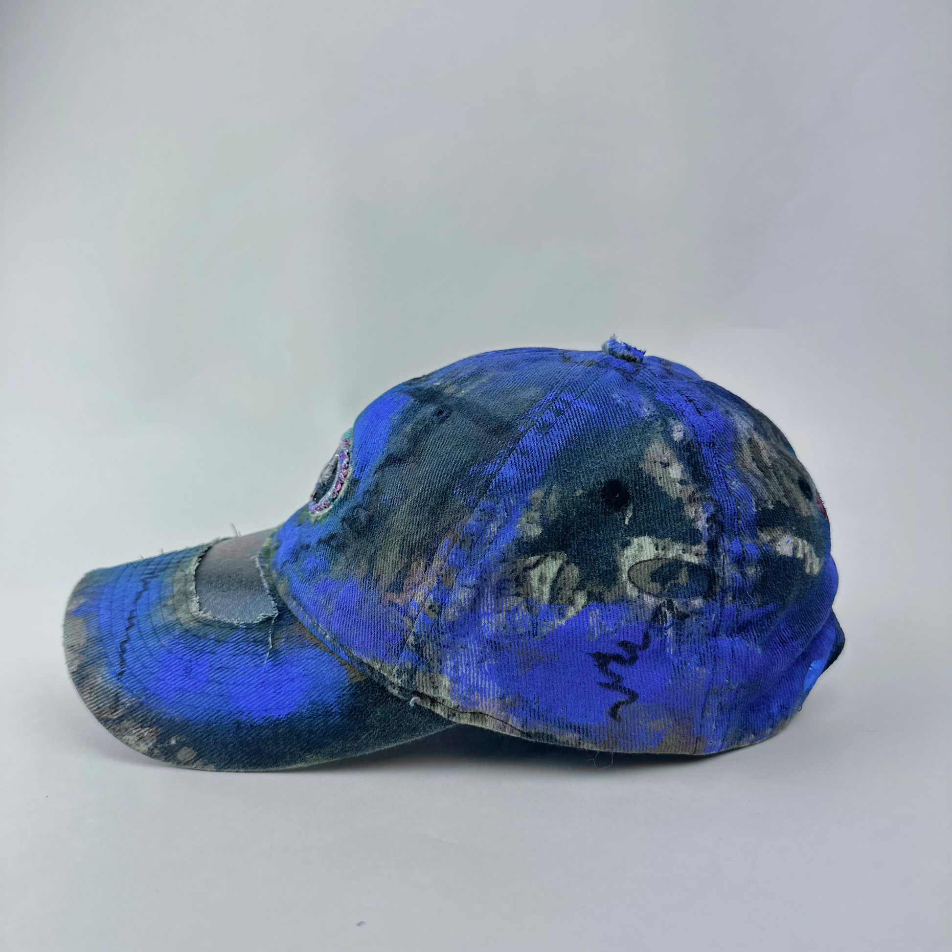 Left side detail of ASTROBOI* x Mossy Oak 'Ultraviolet' showing hand drawn design detail and ultraviolet paint treatment on brown and purple camouflage hat.