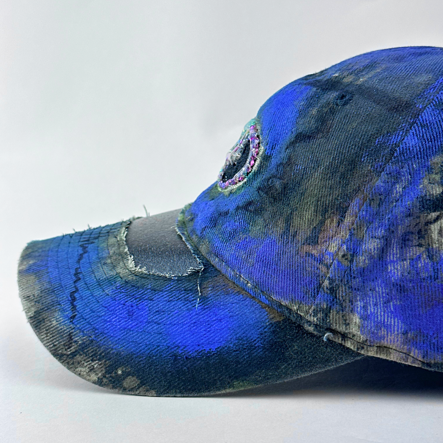 Left side visor detail of ASTROBOI* x Mossy Oak 'Ultraviolet' showing hand drawn design detail and ultraviolet paint treatment on brown and purple camouflage hat.