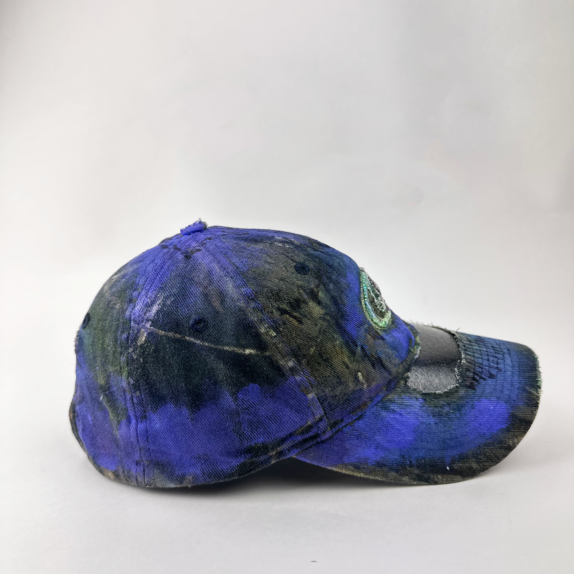 Right side detail of ASTROBOI* x Mossy Oak 'Ultraviolet' showing ultraviolet flowing paint treatment and deconstructed visor on Real Tree camo base.