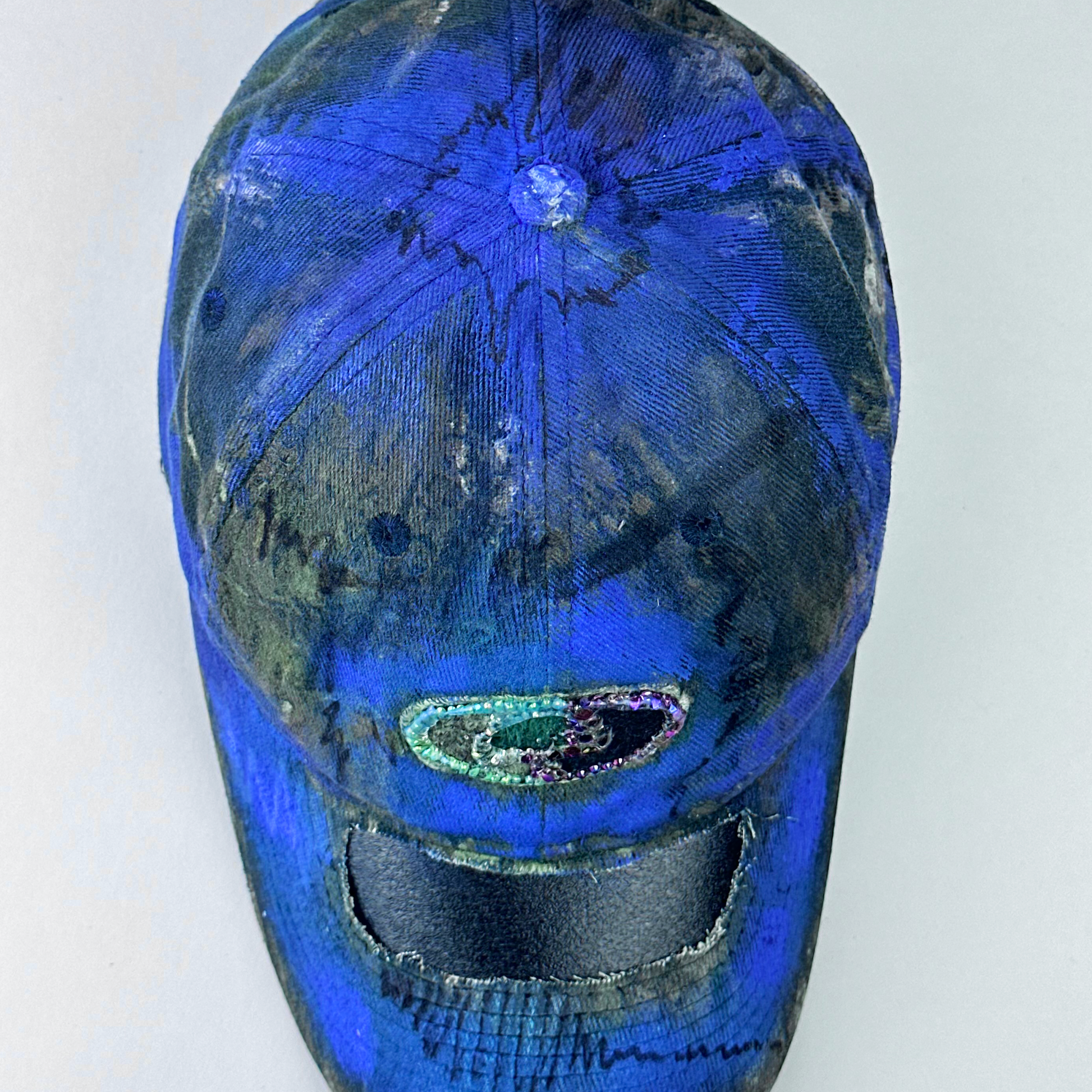 ASTROBOI* x Mossy Oak 'Ultraviolet' brown and purple Real Tree camouflage hat with rhinestone-embellished Mossy Oak logo at front, ultraviolet flowing paint treatment, and deconstructed visor, top view.