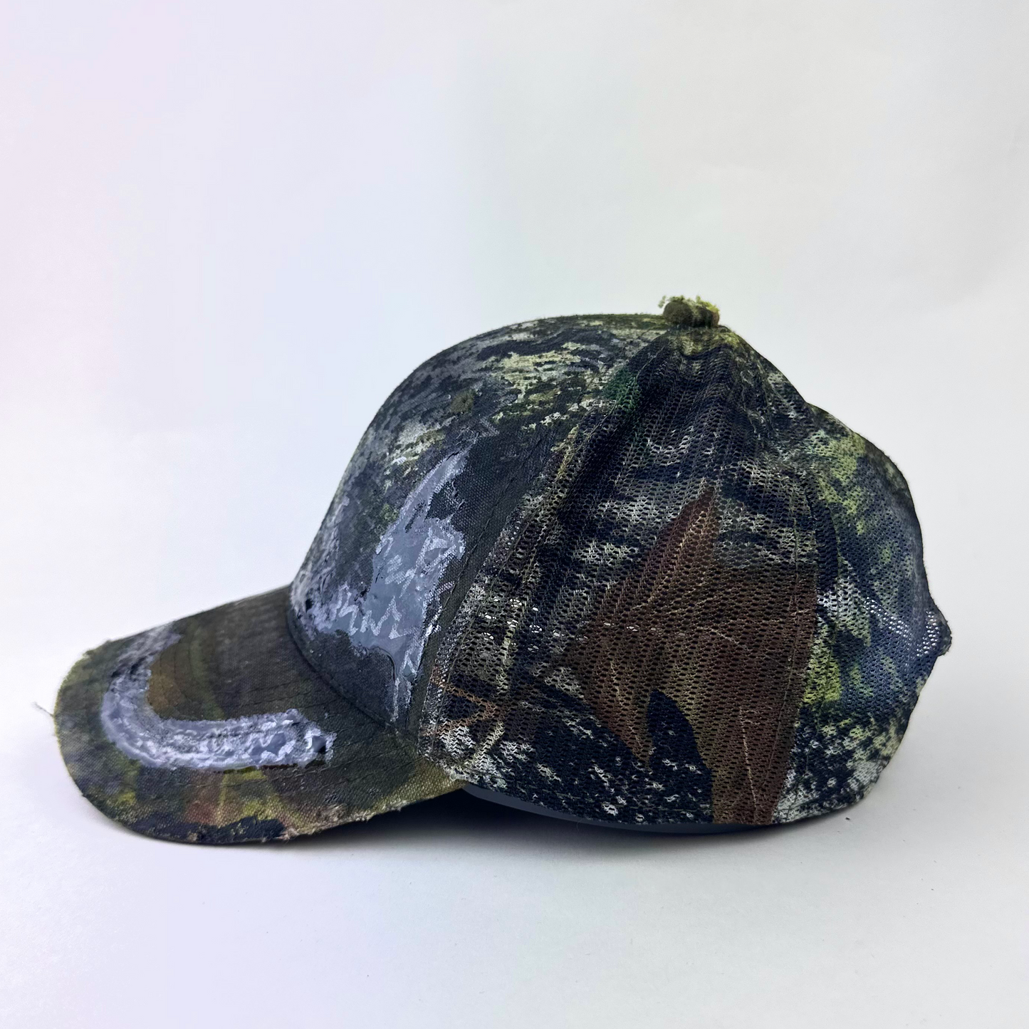 Left side detail of ASTROBOI* 'Mountains' showing hand drawn resin-sealed design and Real Tree camouflage detail on brown trucker hat.