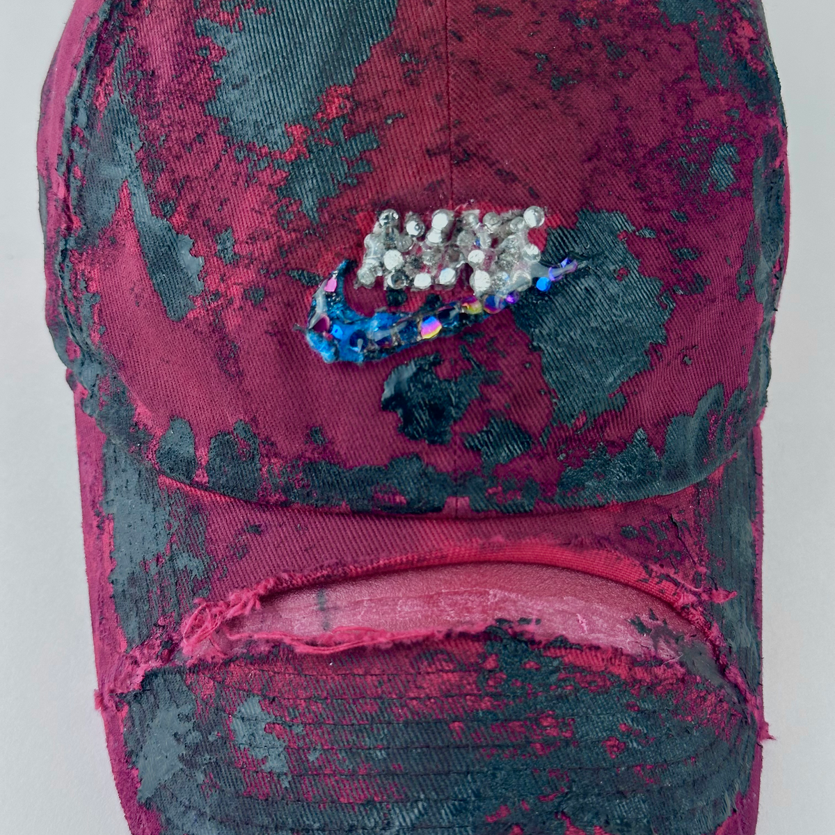 Close-up of ASTROBOI* x Nike 'Comet' showing Nike logo, black painted pattern, and silver and multicolored rhinestones encased in clear resin on distressed red fabric.