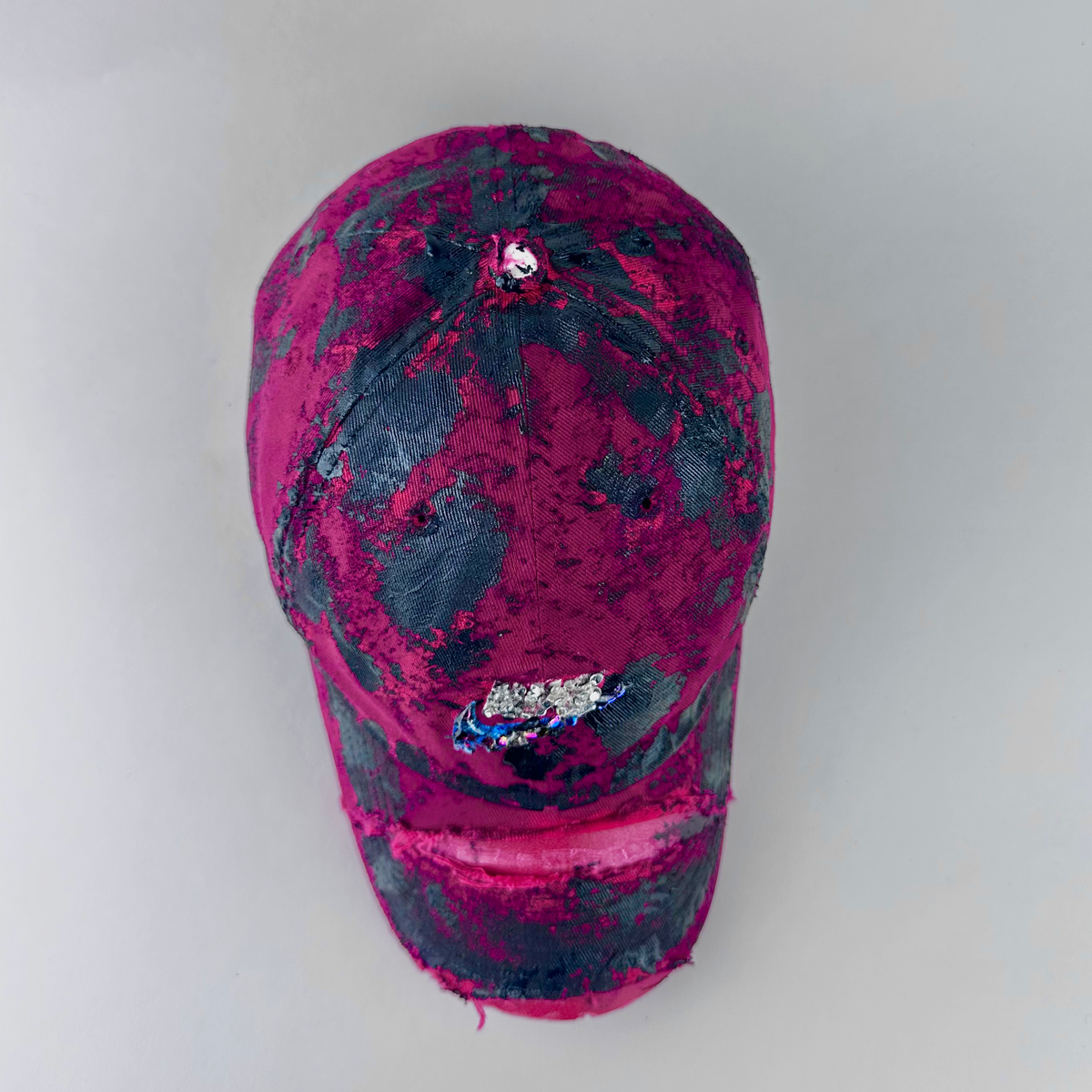 Top view of ASTROBOI* x Nike 'Comet' showing Nike logo, black painted pattern, and silver and multicolored rhinestones encased in clear resin on distressed red fabric.