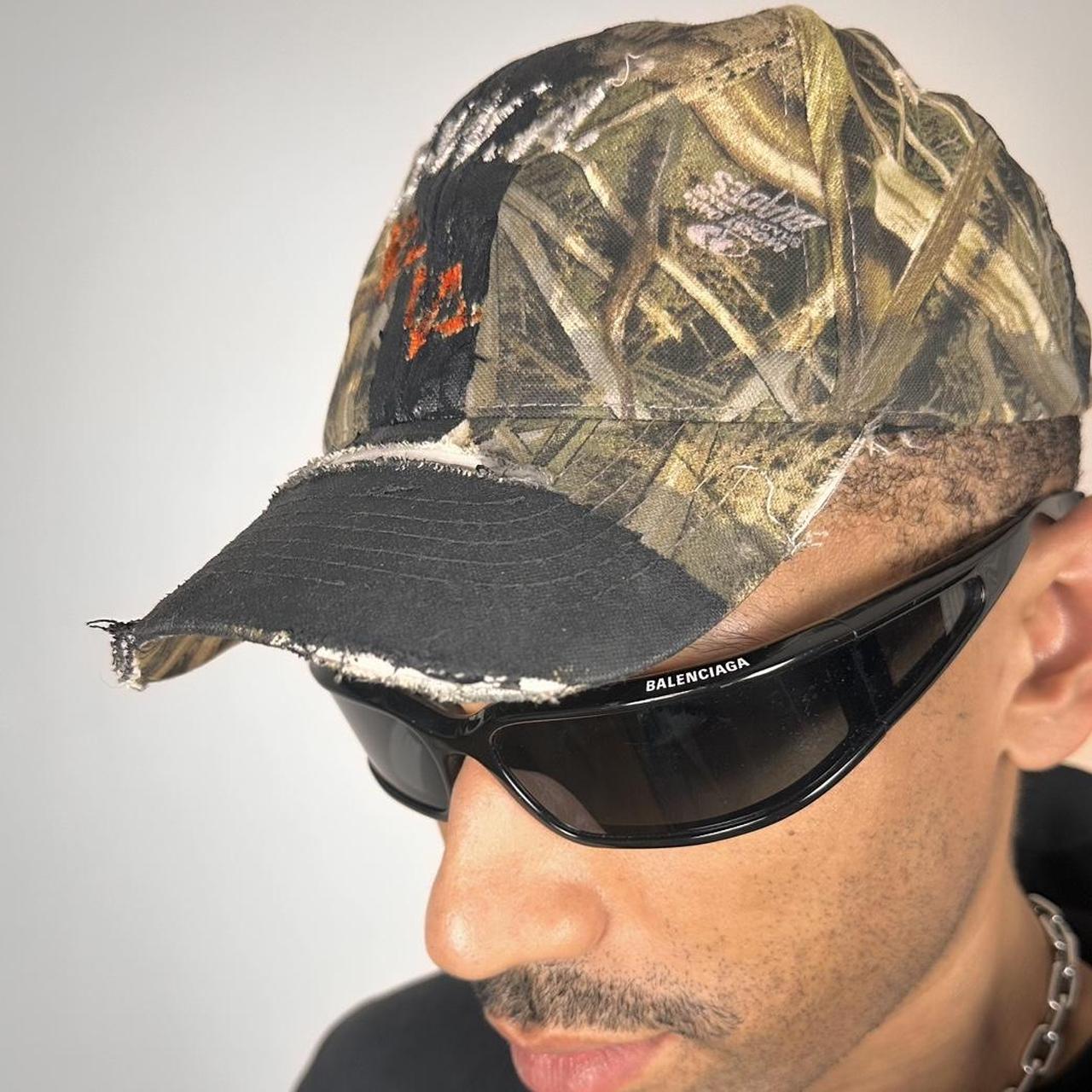 Front left of ASTROBOI* x Mossy Oak brown RealTree camouflage tattoo hat with SWA embroidery, black painted distressing, youth size, custom NYC piece