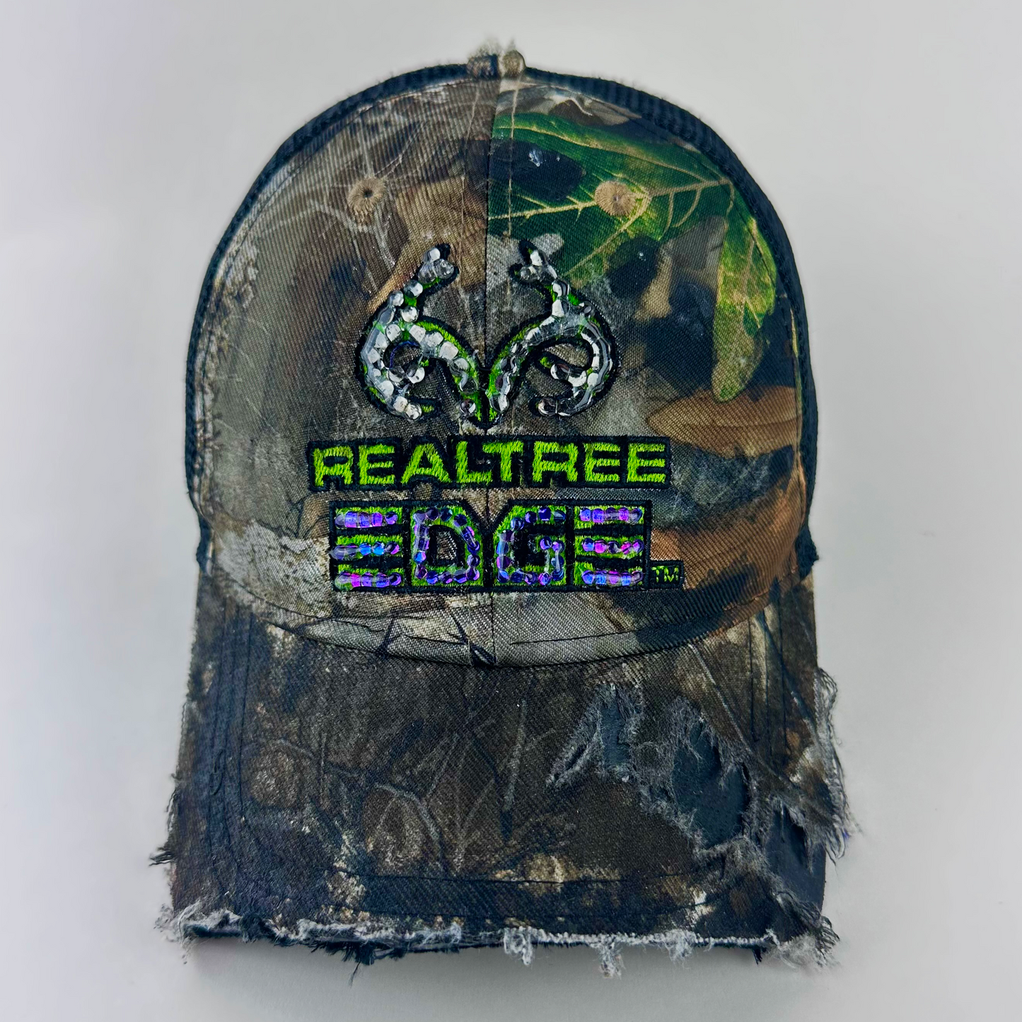 ASTROBOI* x RealTree 'Edge' brown camo rhinestone cap with black and purple/blue rhinestone-embellished RealTree Edge branding across the top and partially sawed-off brim, front view.