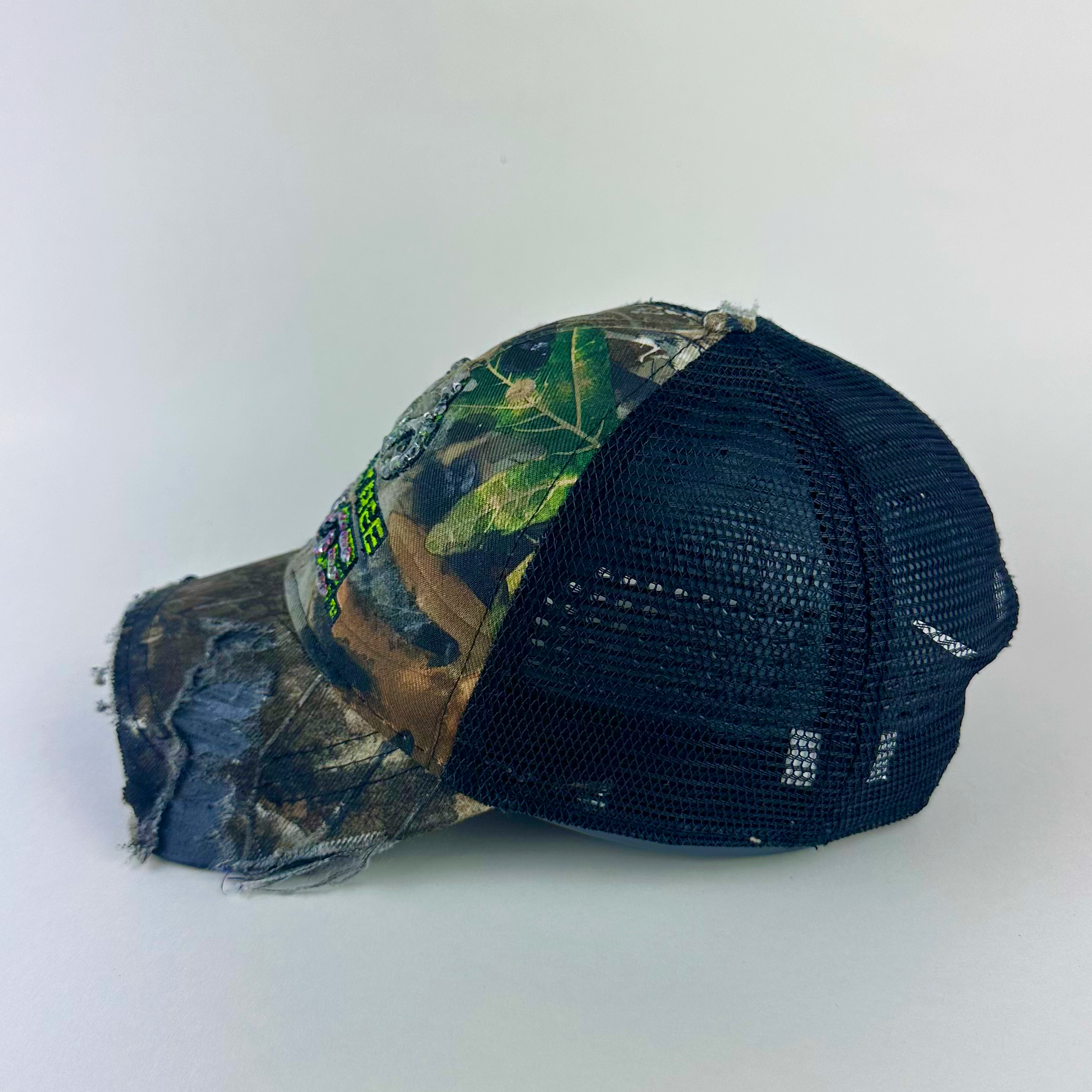 Left side detail of ASTROBOI* x RealTree 'Edge' showing rhinestone embellishment detail and distressed paint treatment on brown RealTree camo cap.