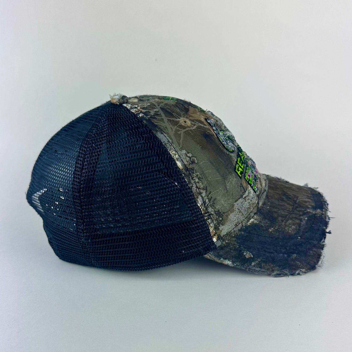 Right side detail of ASTROBOI* x RealTree 'Edge' showing distressing, custom paint treatment, and partially sawed-off brim on brown camo base.