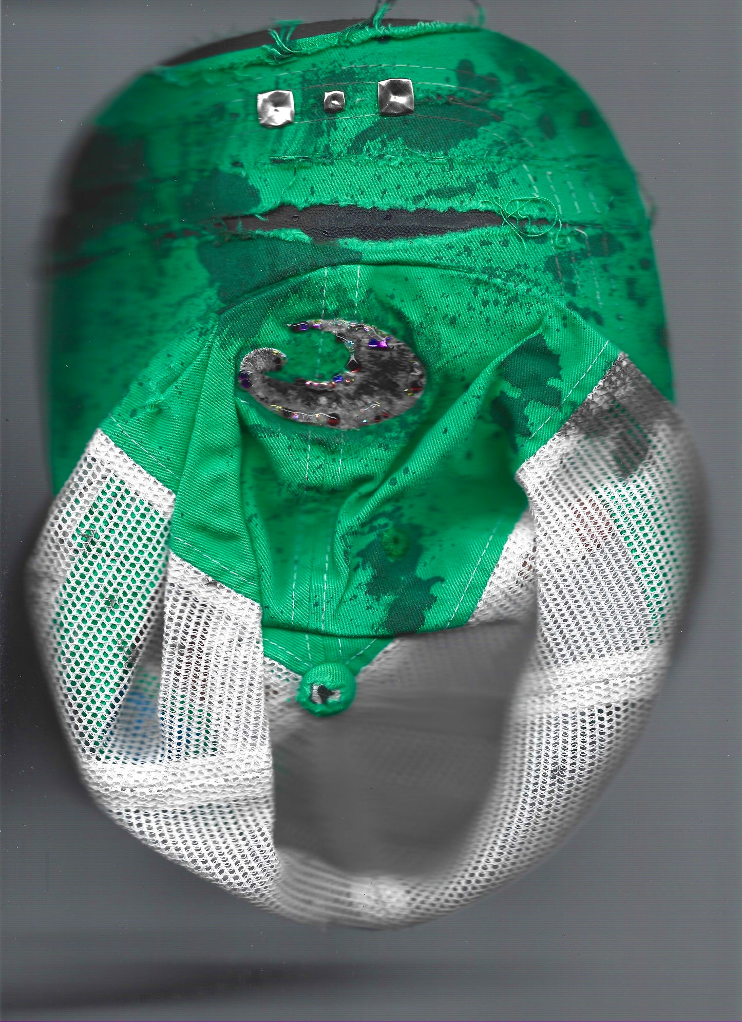 A green and white mesh baseball cap with a black and silver crescent moon patch on the front, photographed against a neutral gray background that has been scanned. 