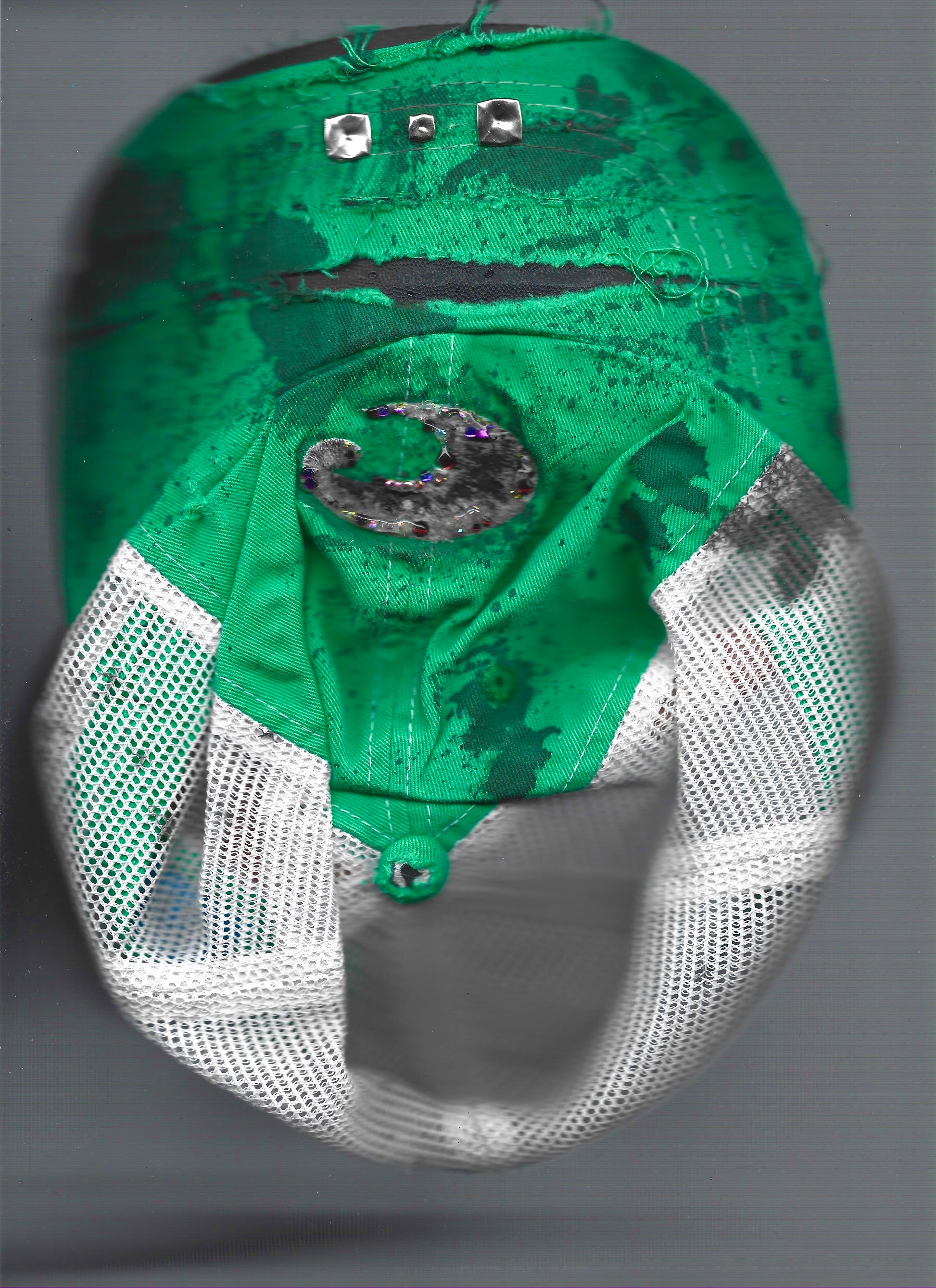 A green and white mesh baseball cap with a black and silver crescent moon patch on the front, photographed against a neutral gray background that has been scanned. 