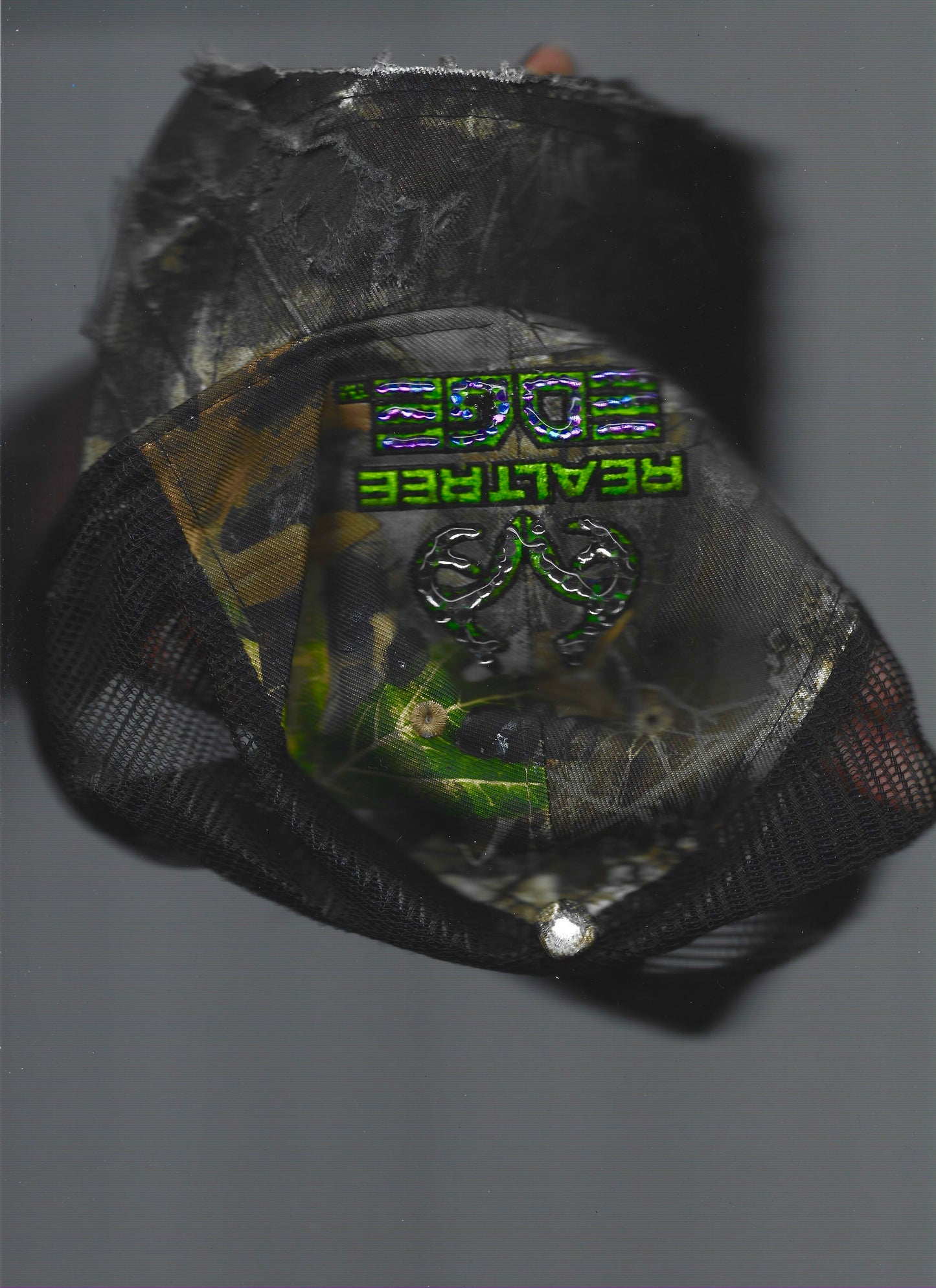 Scanned front view of ASTROBOI* x RealTree 'Edge' brown camo rhinestone cap with black and purple/blue rhinestone-embellished RealTree Edge branding across the top and partially sawed-off brim.