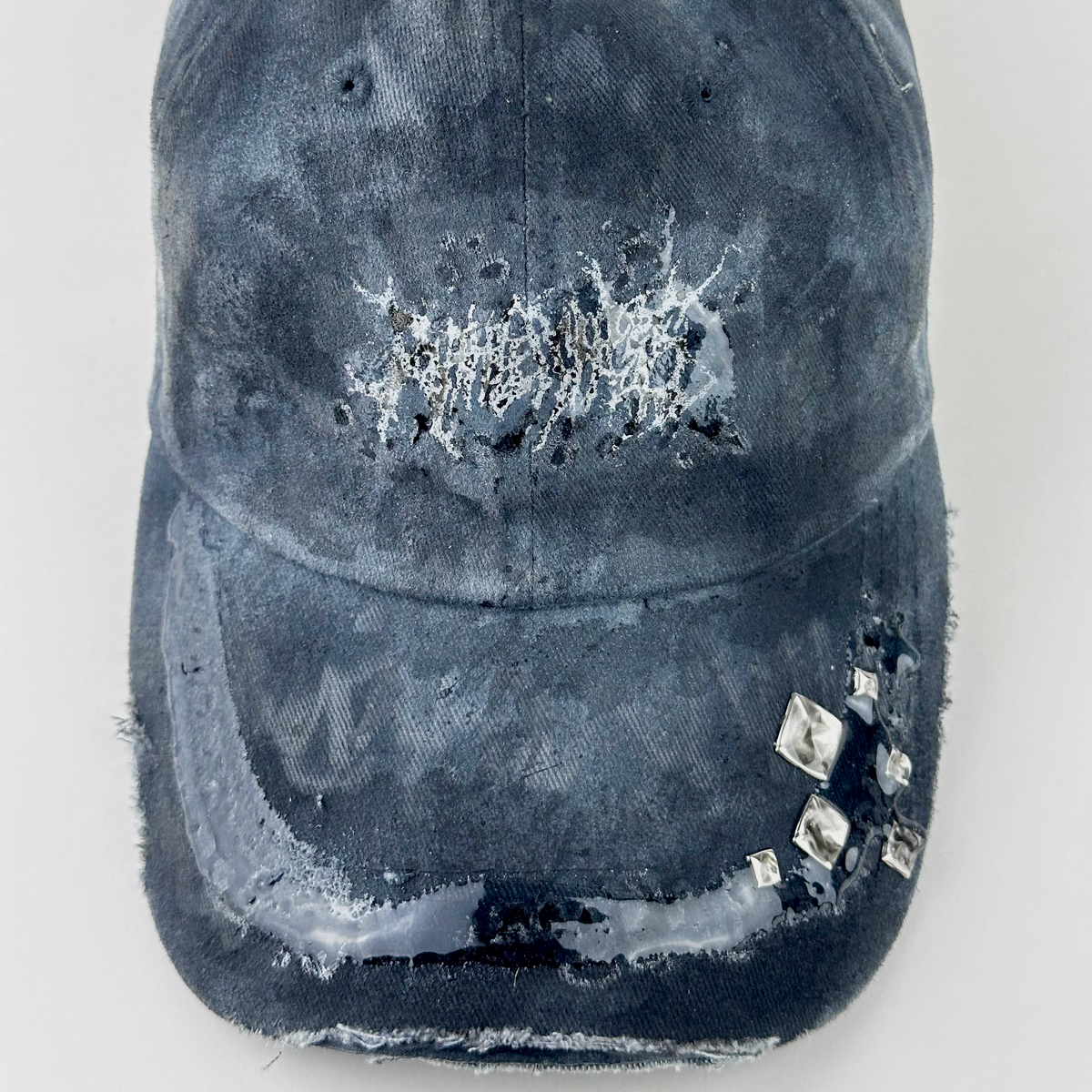 Close-up of ASTROBOI* 'Slick' showing white indie barbed wire logo and silver stud detail on visor sealed under 3D resin coating on black and gray fabric.
