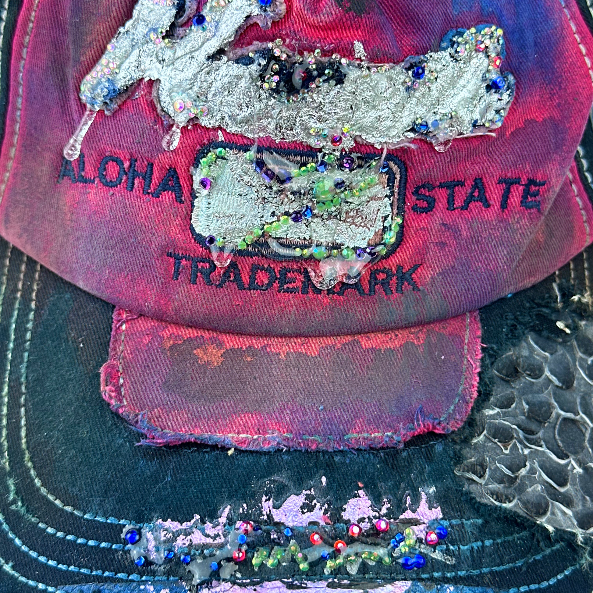Close-up of ASTROBOI* 'Tropicale' showing silver embroidered Hawaii text, rhinestone embellishments, and purple and pink paint splatter with metallic paint detail.