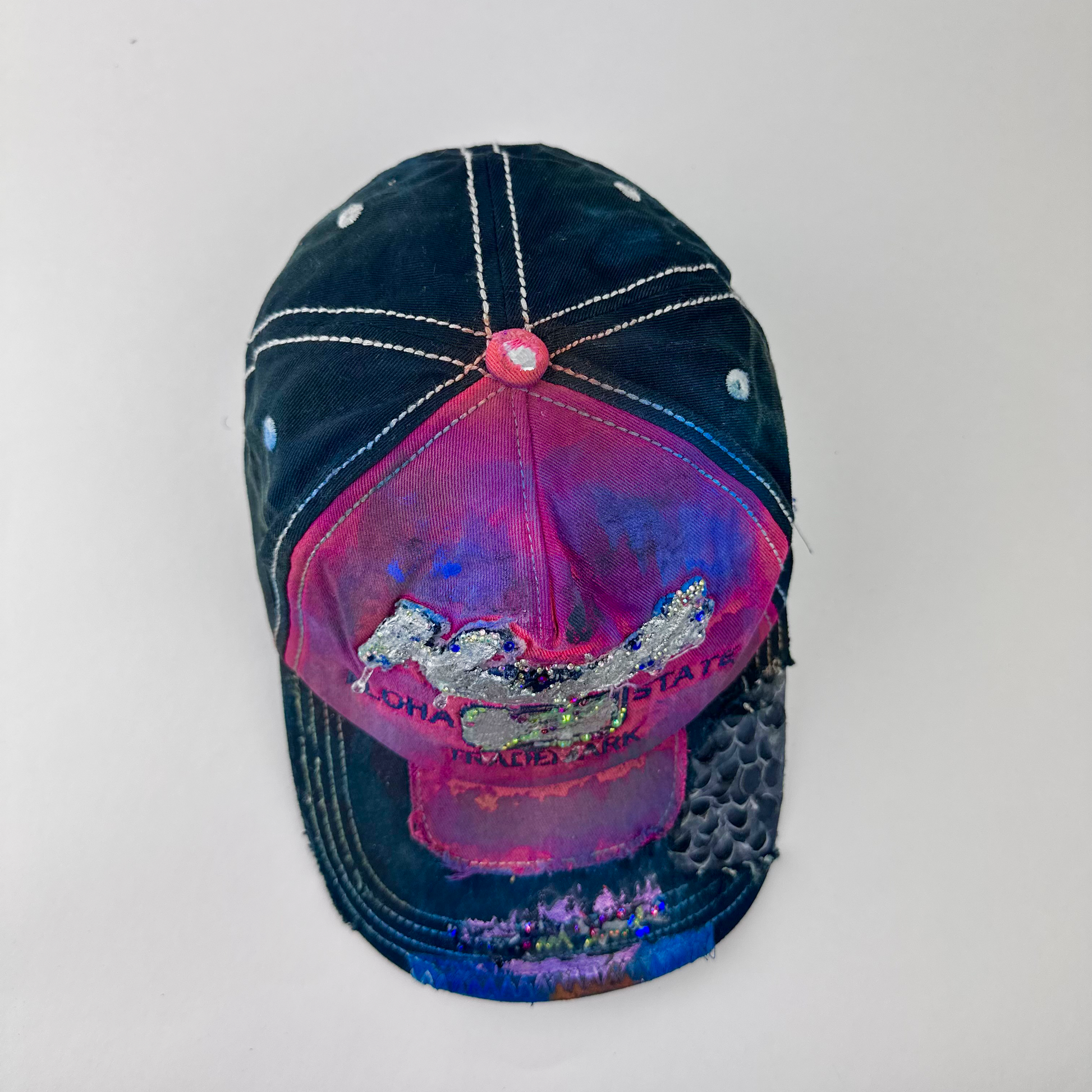 Top view of ASTROBOI* 'Tropicale' showing silver embroidered Hawaii text, rhinestone embellishments, and purple and pink paint splatter with metallic paint detail.