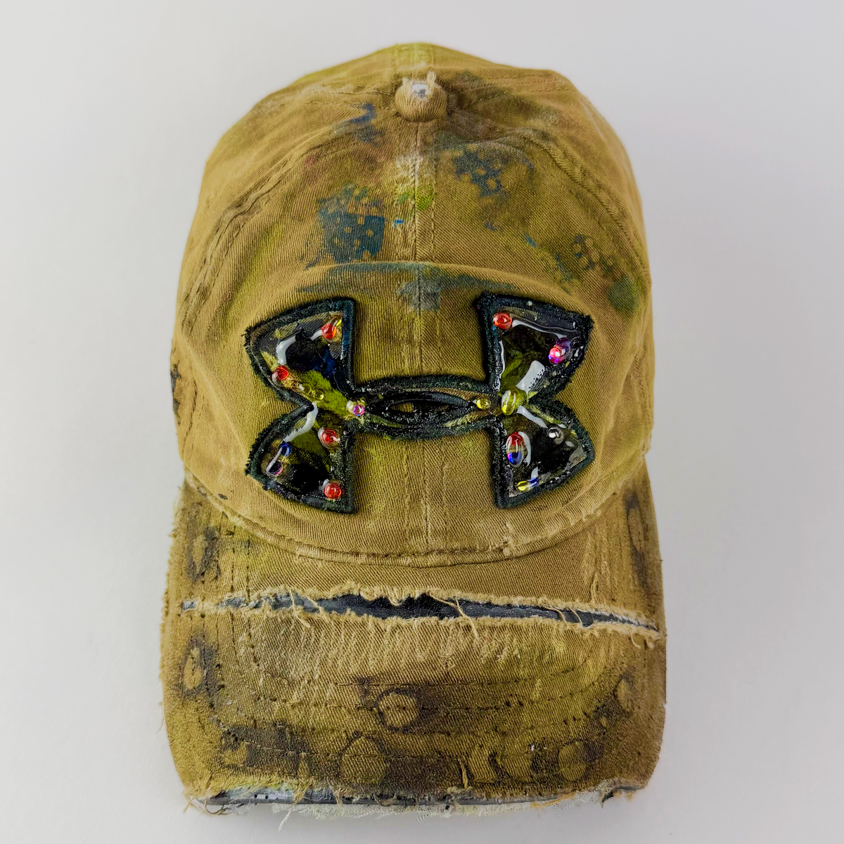 A distressed, washed olive green baseball cap featuring a large, embellished Under Armour logo on the front with rhinestones, set against a plain light gray background.