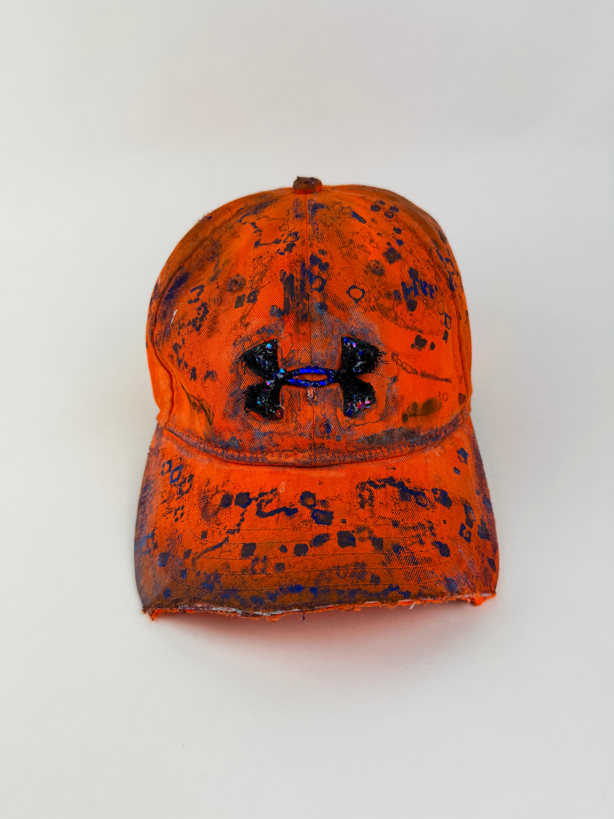 ASTROBOI* x Under Armour ‘Solar Flare’ orange and blue futuristic rhinestone cap with hand drawn blue abstract design, rhinestone-embellished frayed logo, and partially sawed-off visor, front view.