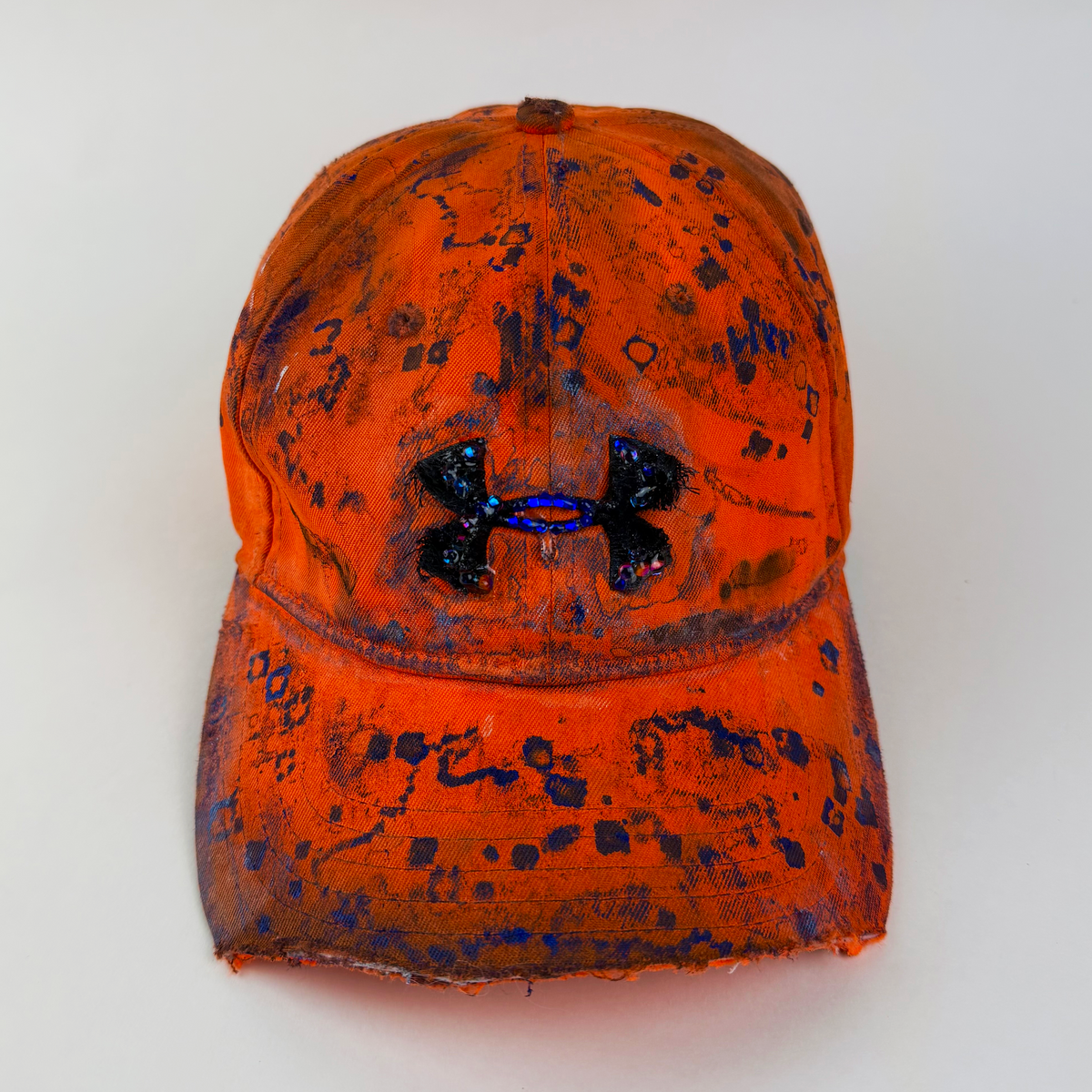 ASTROBOI* x Under Armour ‘Solar Flare’ orange and blue futuristic rhinestone cap with hand drawn blue abstract design, rhinestone-embellished frayed logo, and partially sawed-off visor, front view.