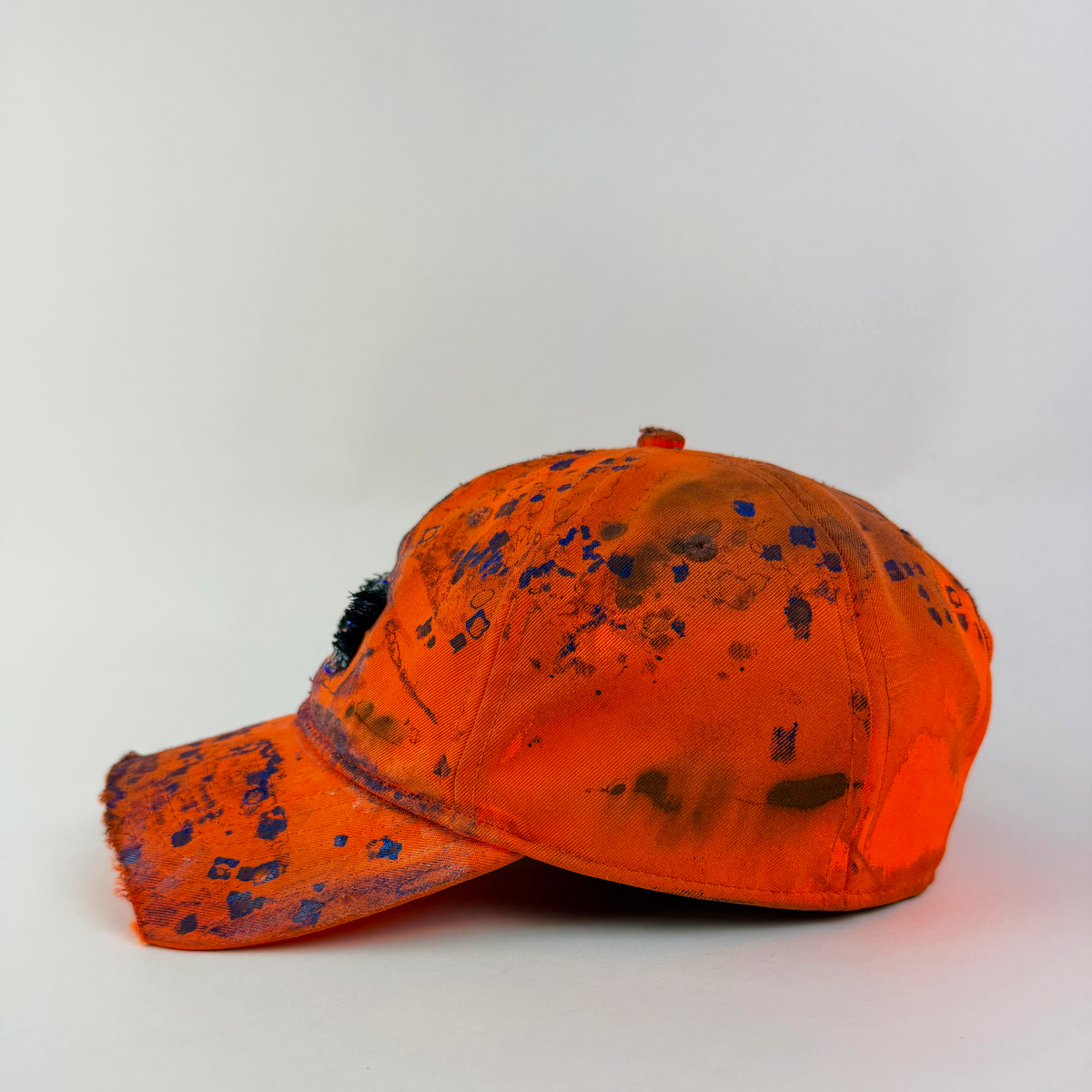 Left side detail of ASTROBOI* x Under Armour ‘Solar Flare’ showing blue abstract design, faded appearance, and partially sawed-off visor on orange cap.