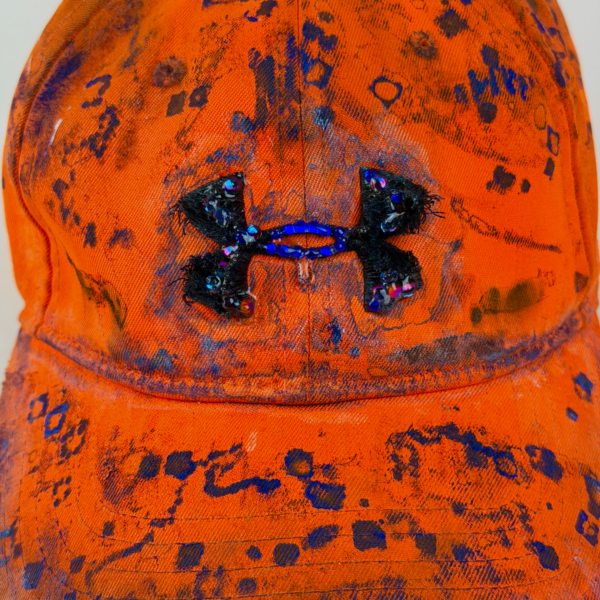 Close-up of an orange Under Armour baseball cap with a distressed, paint-splatter style finish and a black Under Armour logo patch on the front.