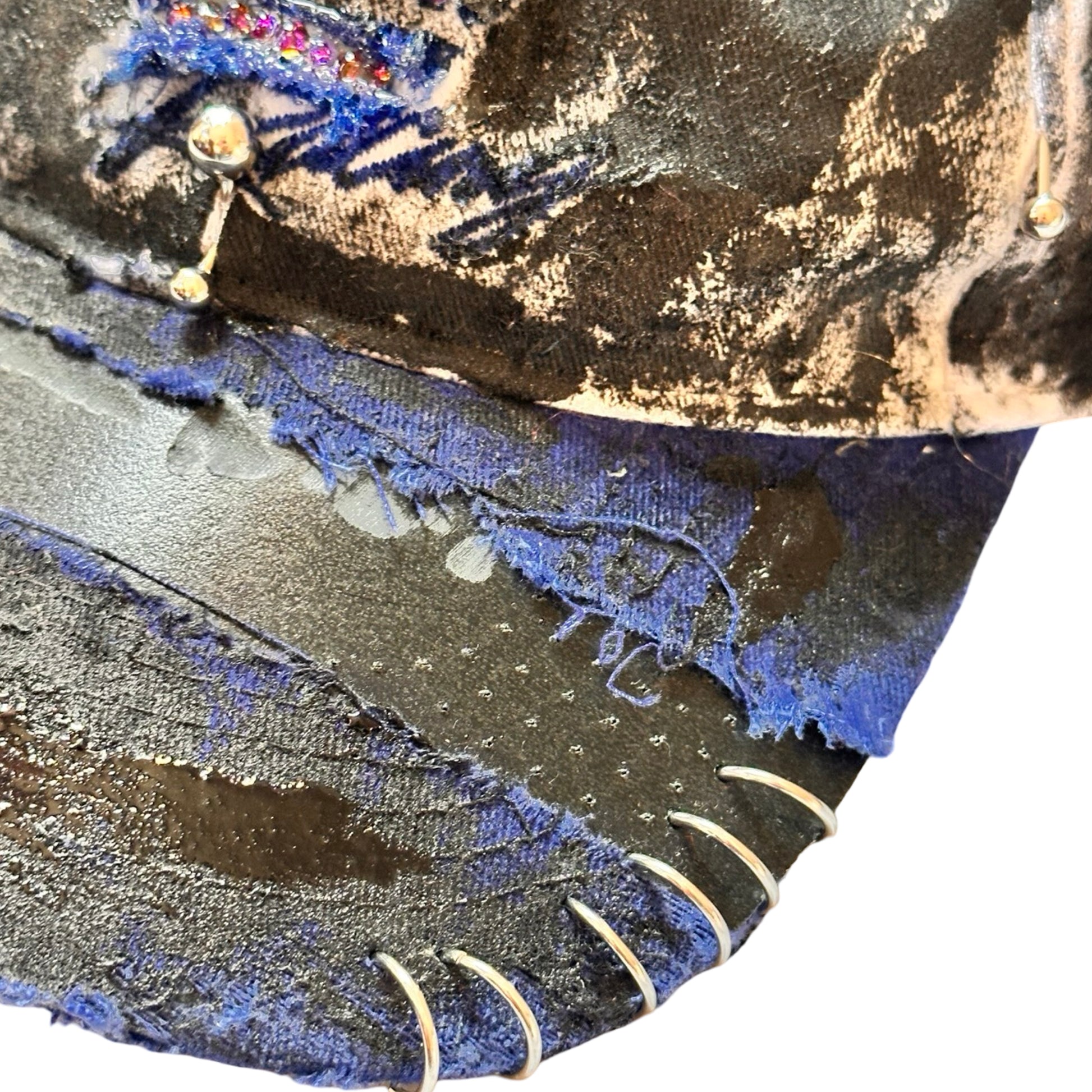 Flat front visor detail of Blue and white ASTROBOI* NAPA hat with rhinestone-covered logo sealed in clear resin, stainless steel piercings, and a deconstructed visor, handcrafted in NYC.