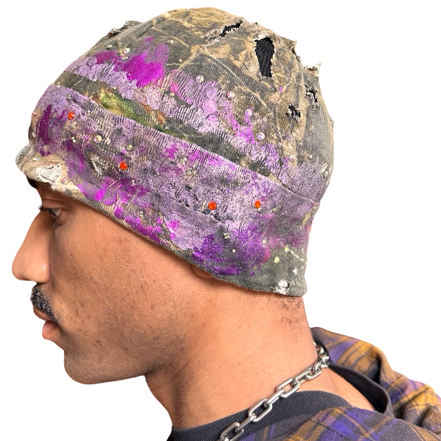 Left side of ASTROBOI* brown RealTree grunge beanie with ripped details, lavender and magenta paint, and colorful rhinestones, handmade in NYC.