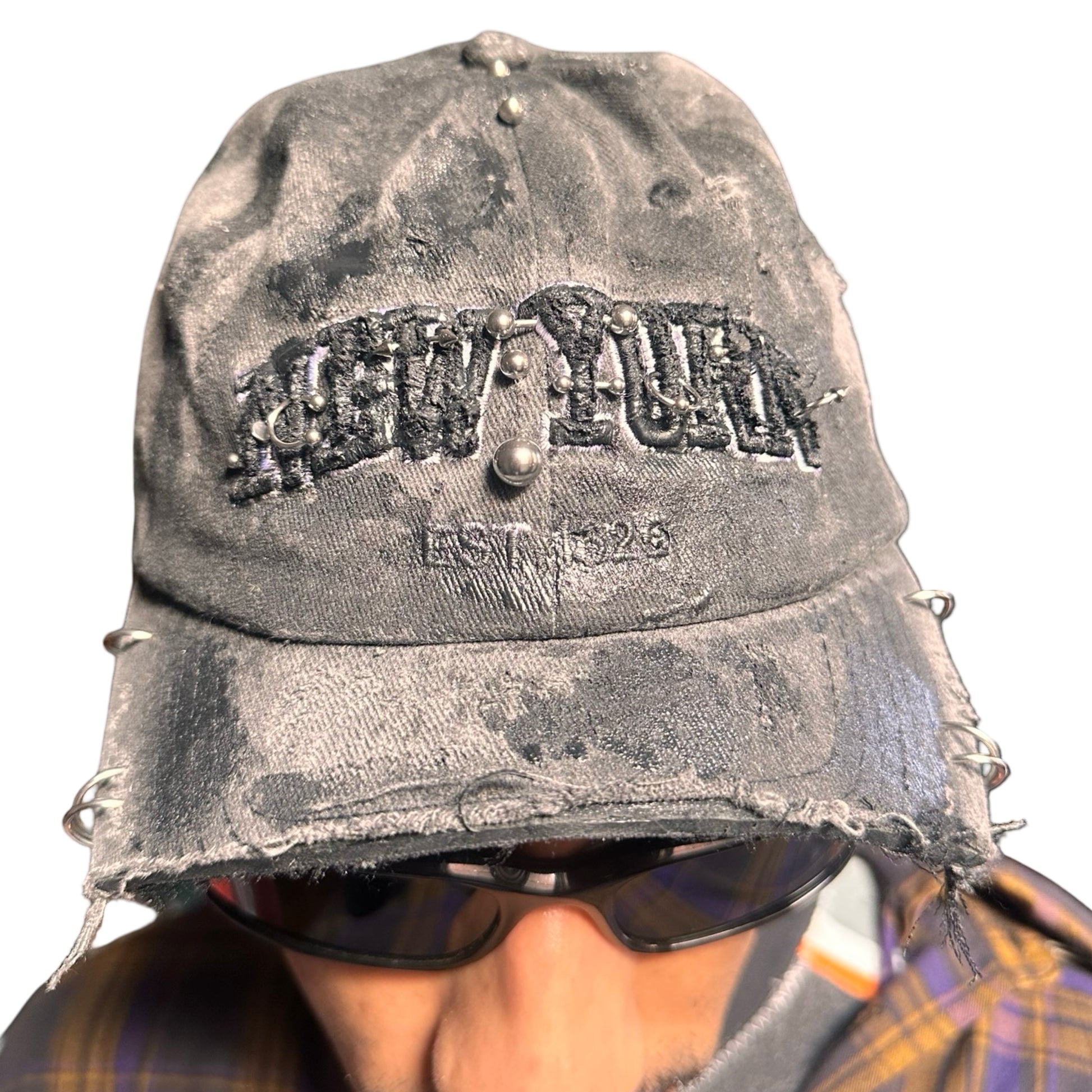 Front 2 of Black half-visor “New York” hat with embroidered front logo, stainless steel piercings, and an adjustable strap.