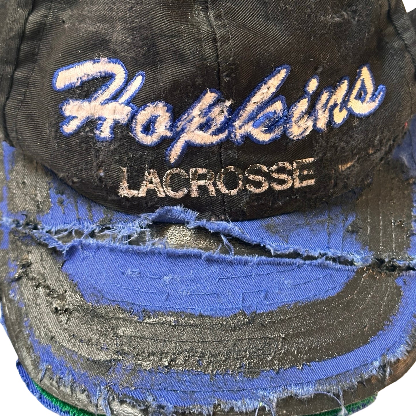 Flat close up of Black distressed ASTROBOI* Hopkins Lacrosse cap with blue embroidery and custom black paint treatment, snapback style, handcrafted in NYC.