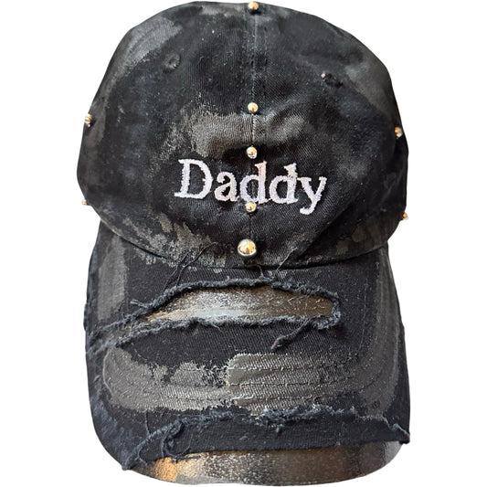 Flat front of Black distressed ASTROBOI* ‘Daddy’ hat with custom paint detailing and stainless steel piercings, handcrafted in NYC.