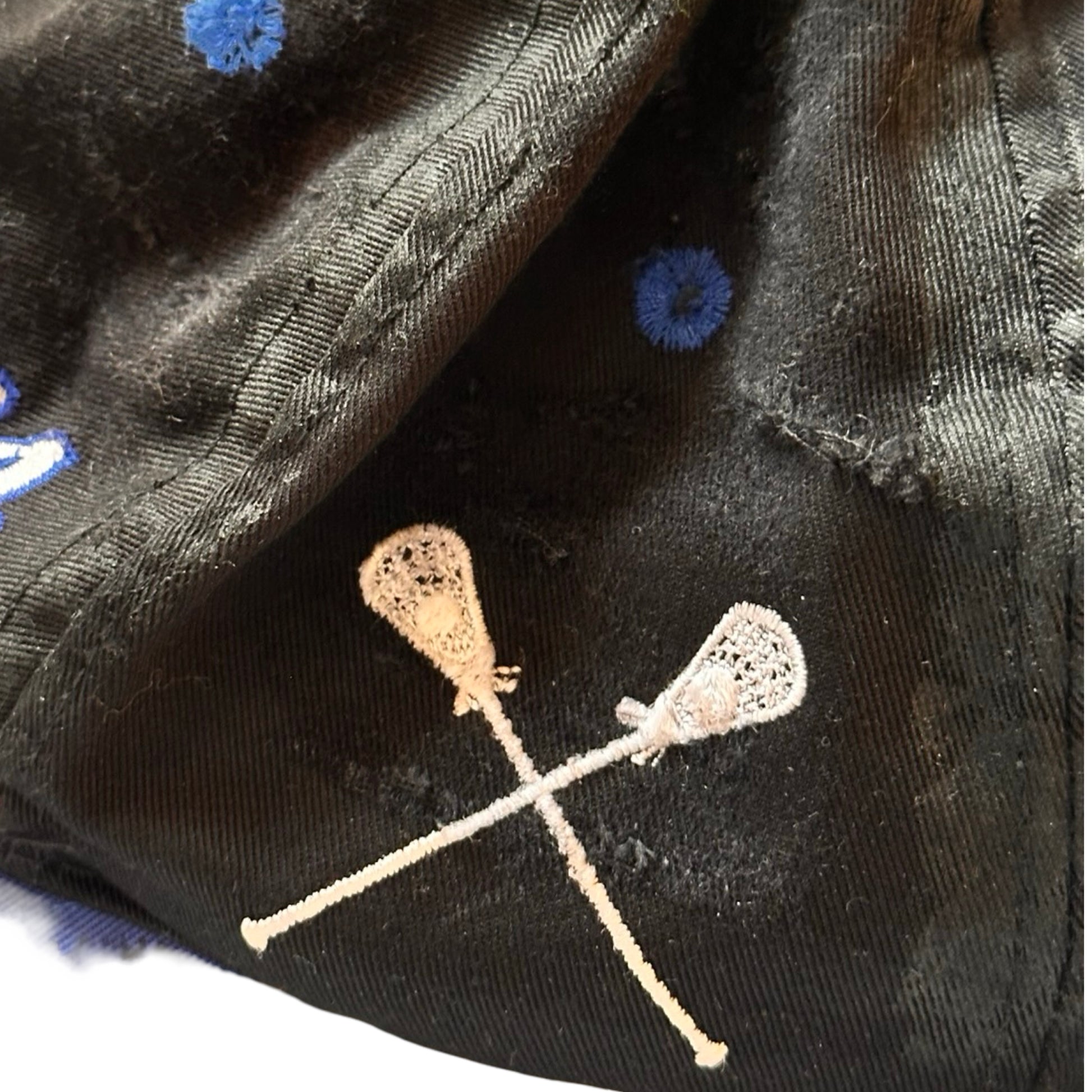 Flat side detail Black distressed ASTROBOI* Hopkins Lacrosse cap with blue embroidery and custom black paint treatment, snapback style, handcrafted in NYC.