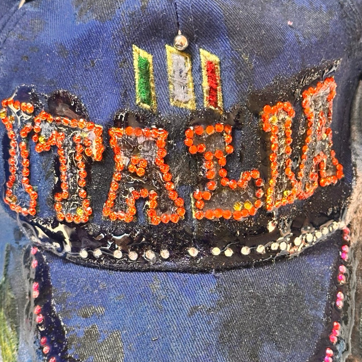 Flat close up of Upcycled blue and white ASTROBOI* ‘ITALIA’ hat with rhinestones, resin, custom paint, and stainless steel piercings, handcrafted in NYC.