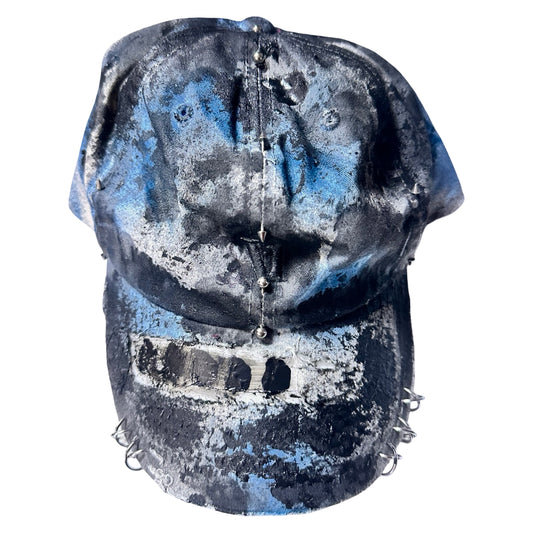 Front flat of Black Vuori baseball hat customized by ASTROBOI* with blue and black painted details, stainless steel piercings, and an embroidered V logo.